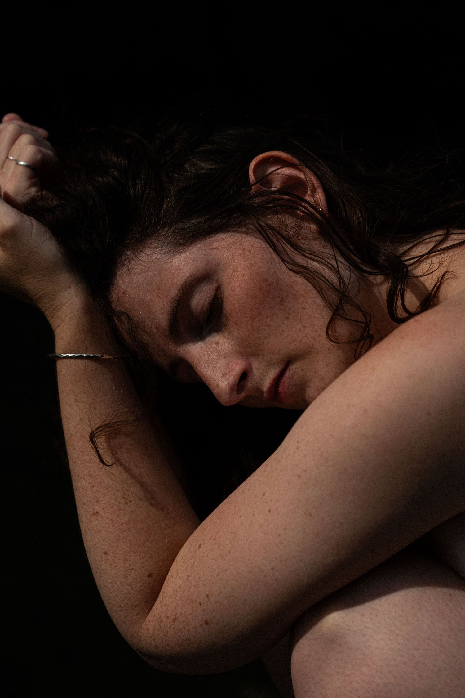 Close-up portrait of woman with wet hair resting on arms against black background.