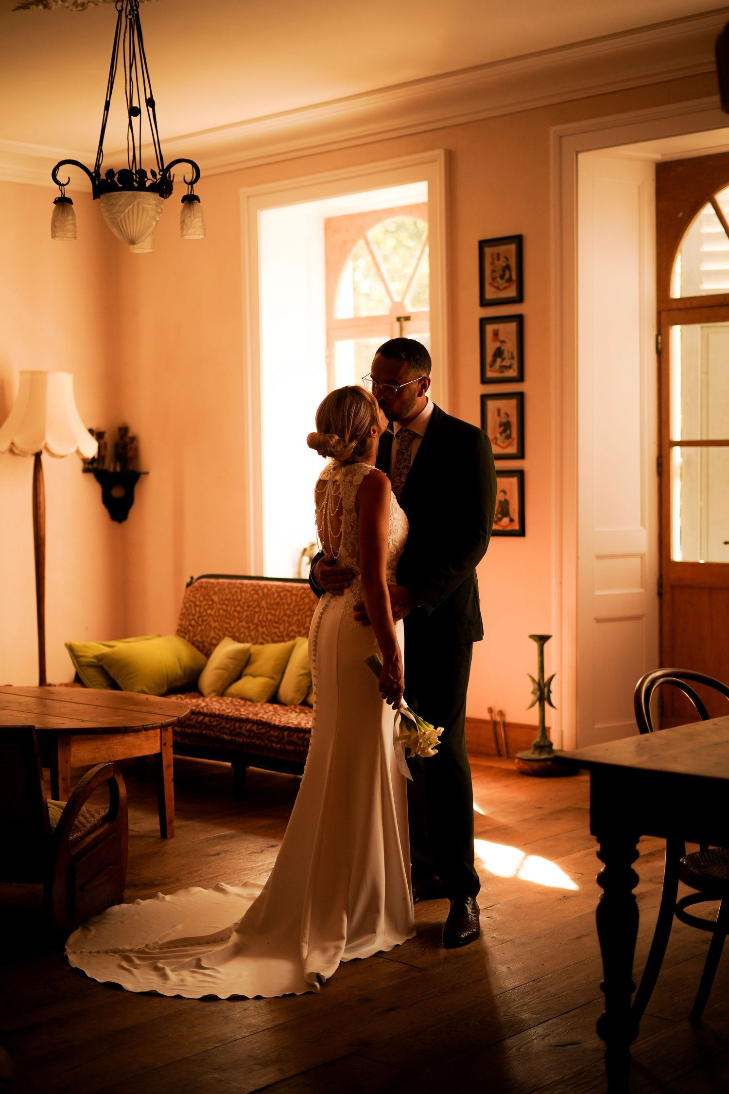 Bride and groom share a romantic kiss in warmly lit vintage interior room.