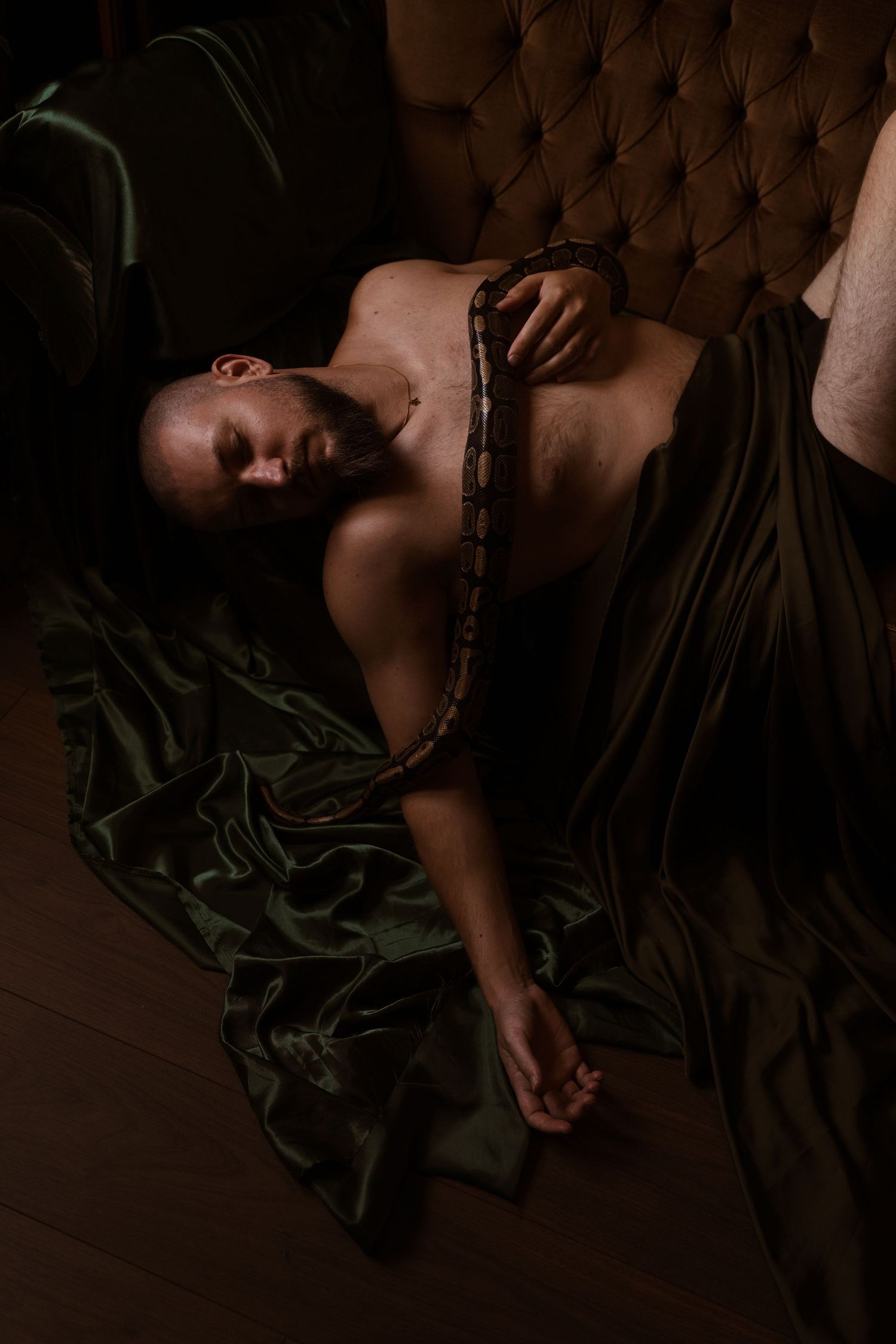 Shirtless man with a large snake draped over him on green silk fabric.