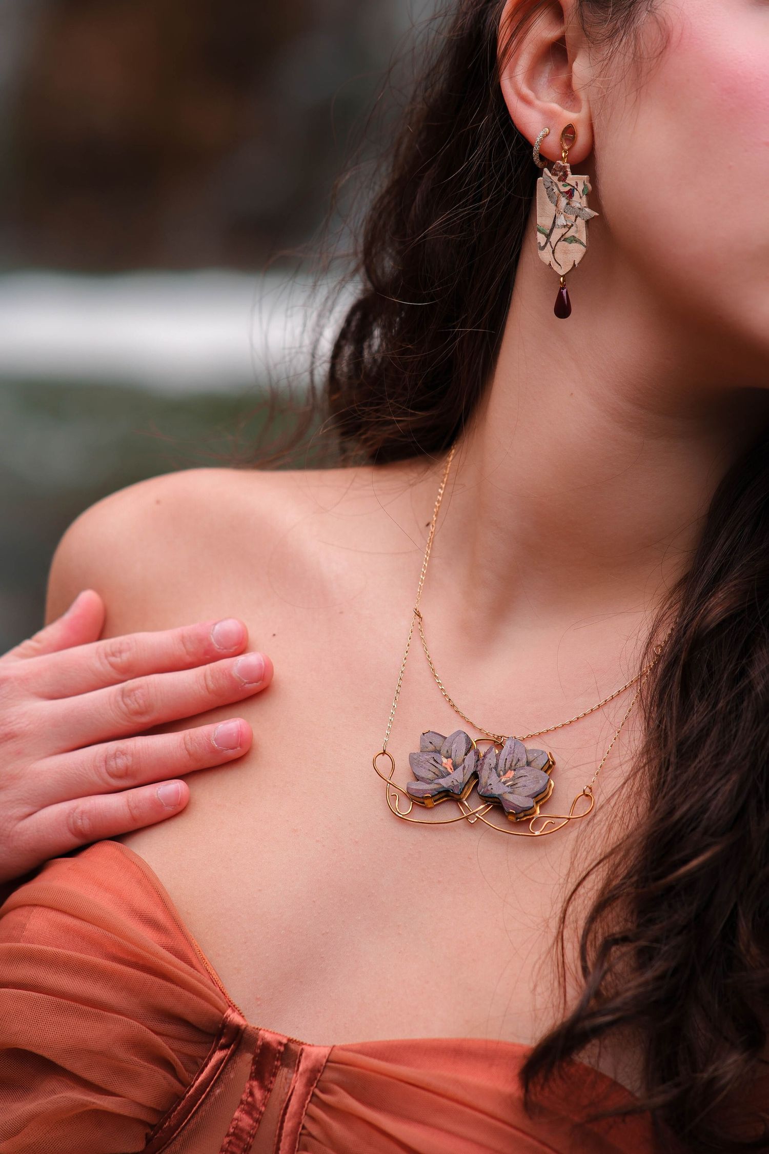 Close-up of woman wearing floral necklace and earrings in an orange off-shoulder dress.