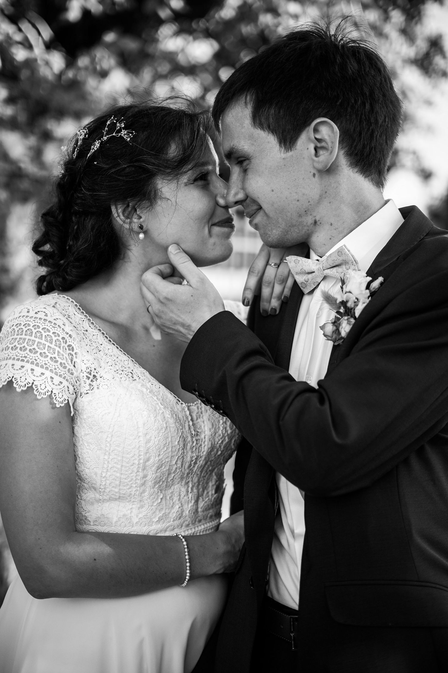 Black and white portrait of bride and groom sharing tender moment outdoors before wedding.