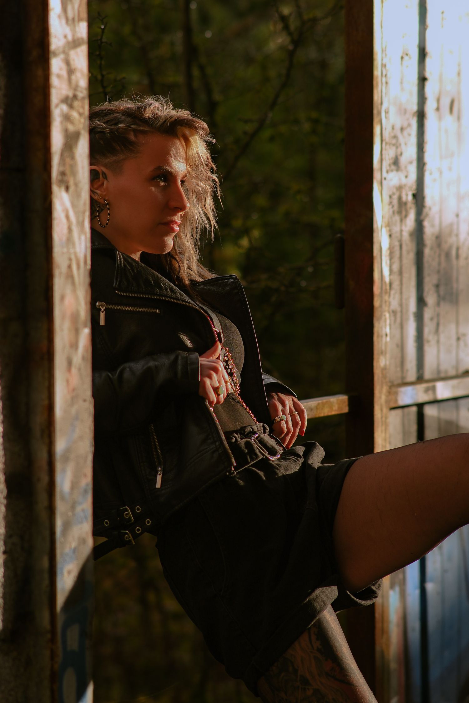 Edgy woman in black leather jacket sitting in an abandoned structure with moody lighting.