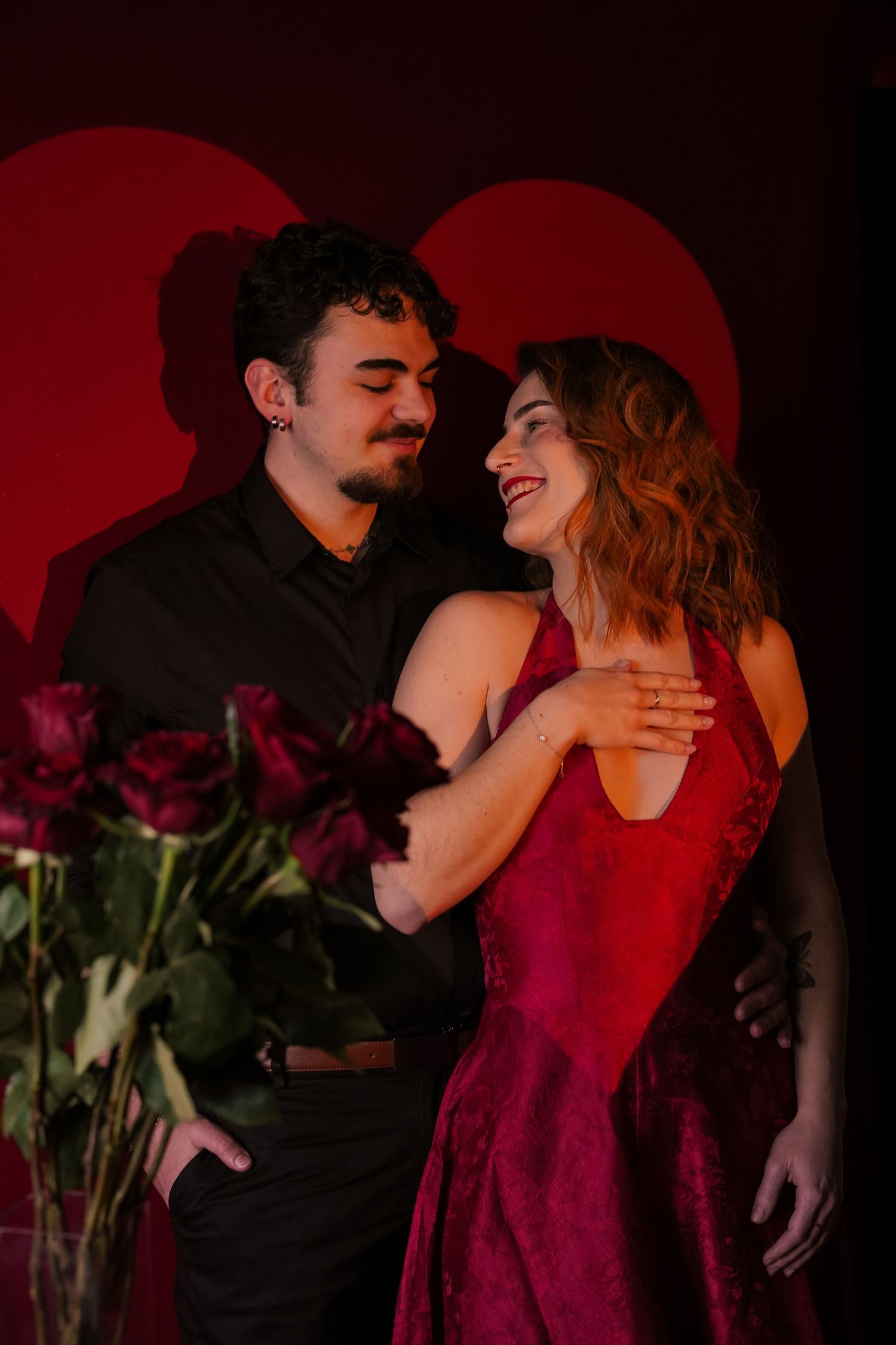 Young couple embracing near red roses with heart-shaped backdrop on Valentines Day.