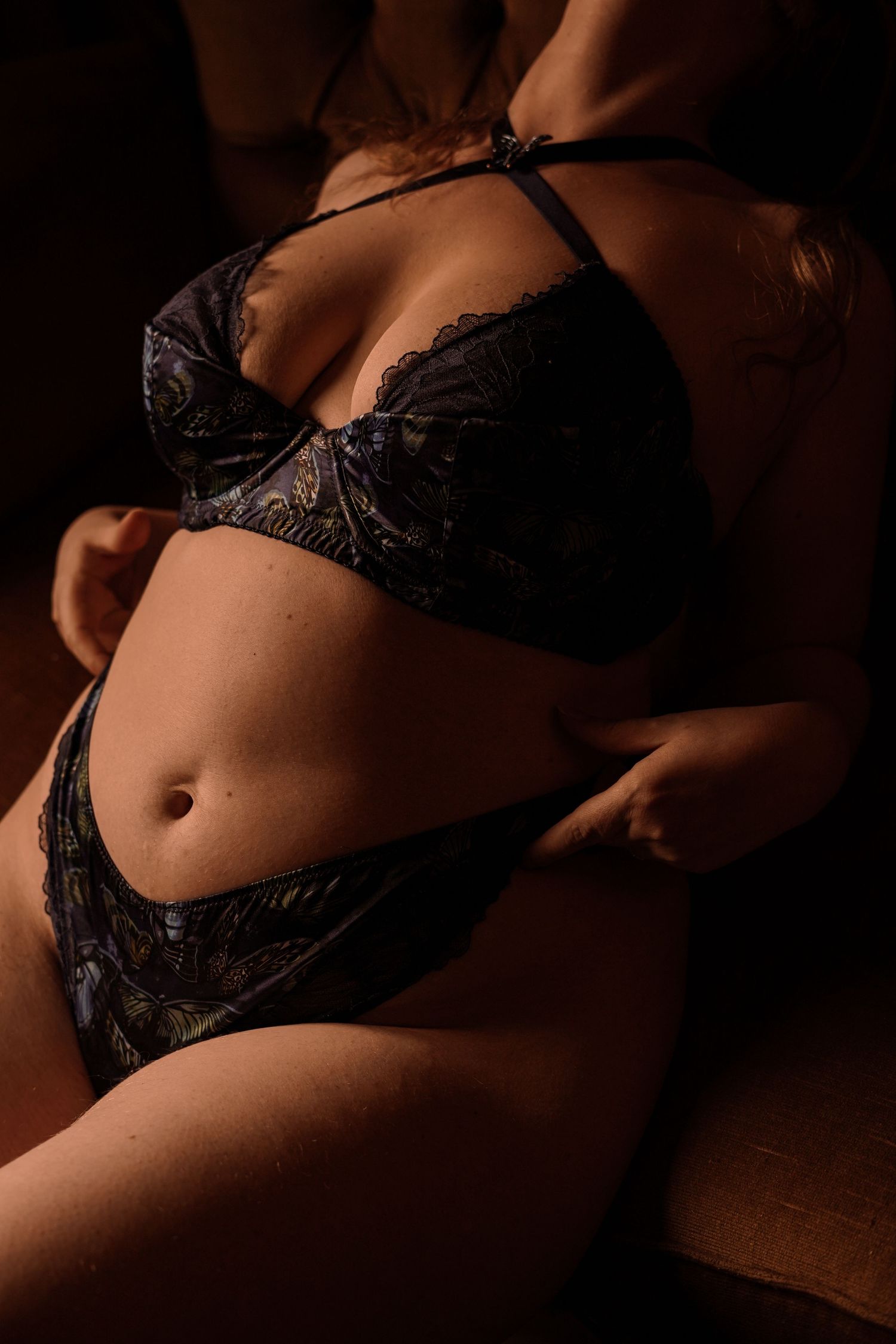 A woman in patterned lace lingerie set poses in warm, moody boudoir photography lighting.