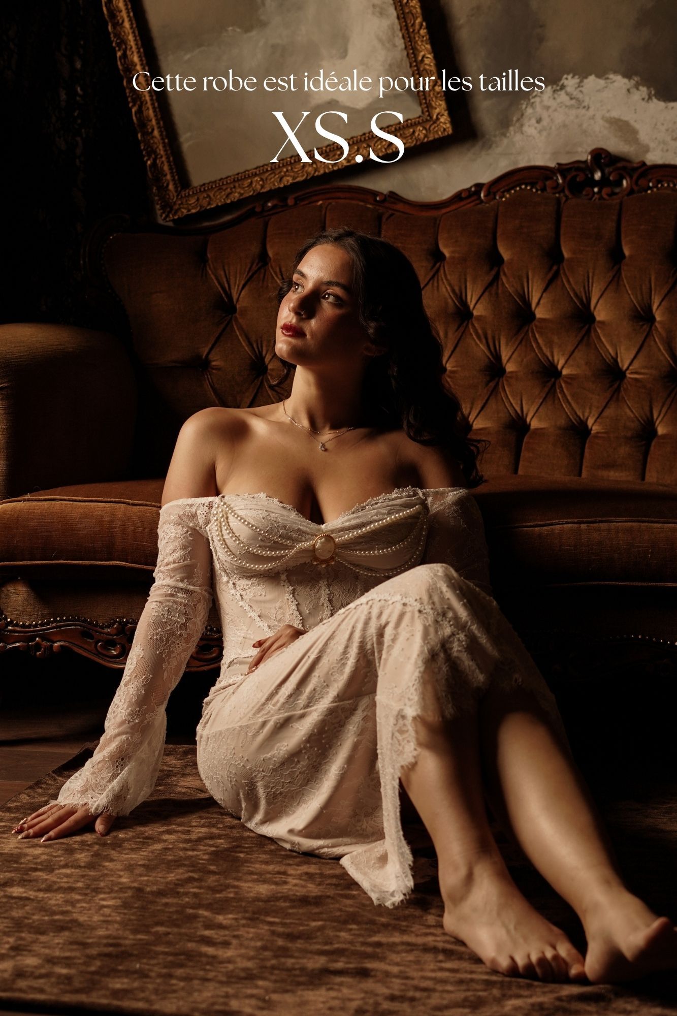 Woman in white lace off-shoulder gown sitting on floor beside velvet sofa, ideal for XS and S sizes.