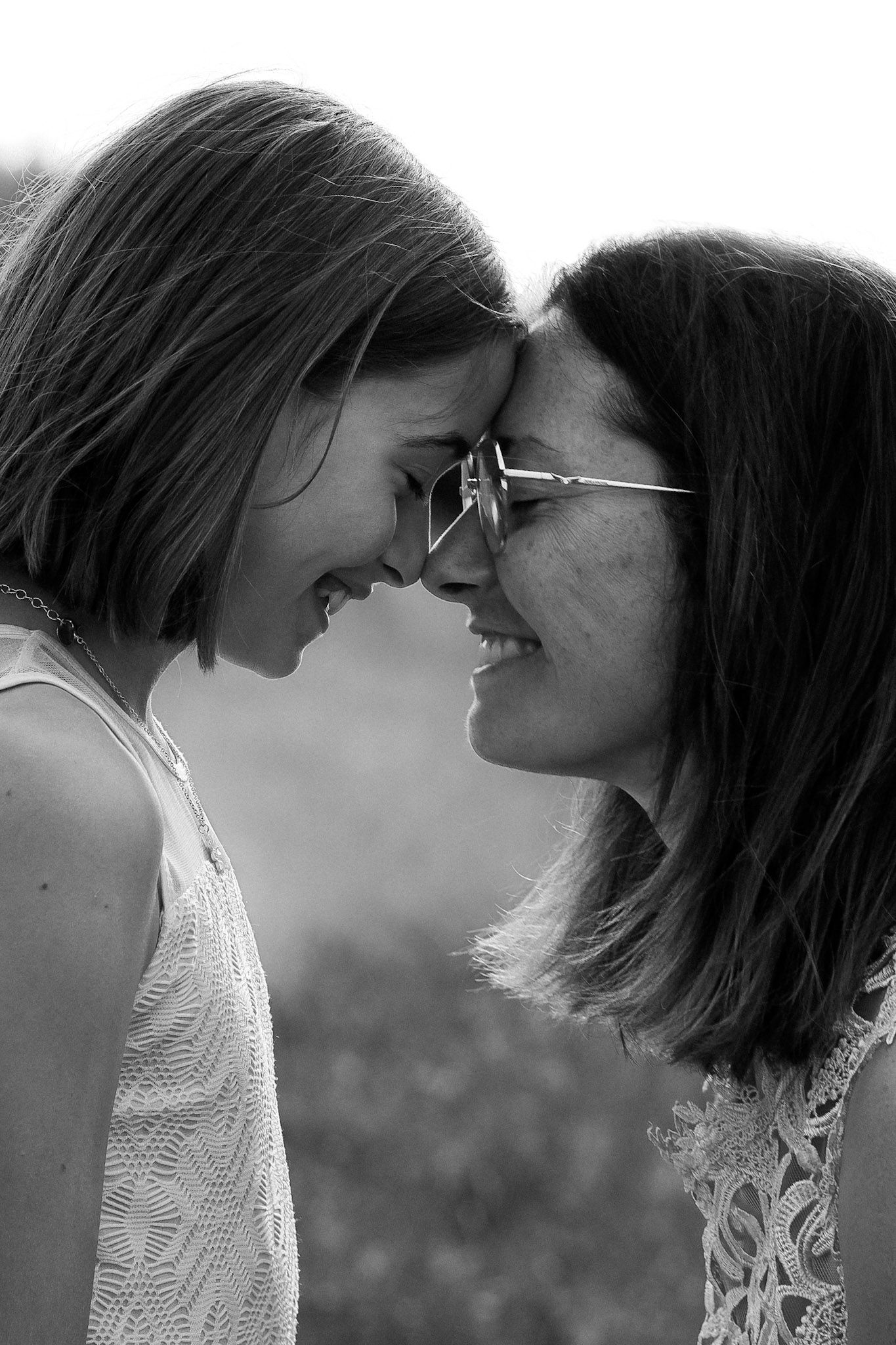 Black and white photo of two women smiling and touching foreheads in a tender, joyful moment outdoors.