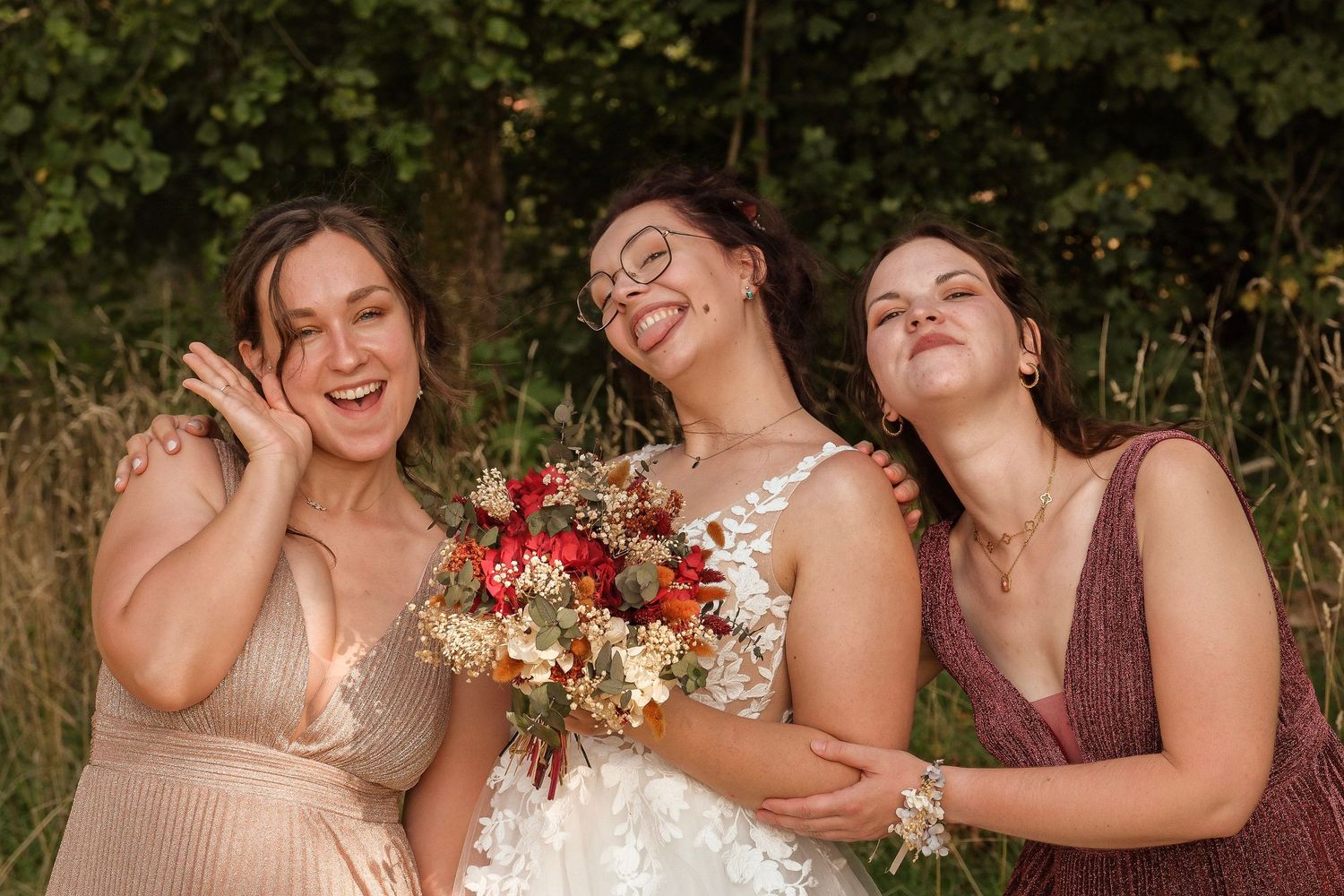 Joyful bride holding a colorful bouquet laughs with two bridesmaids in a lush garden setting.