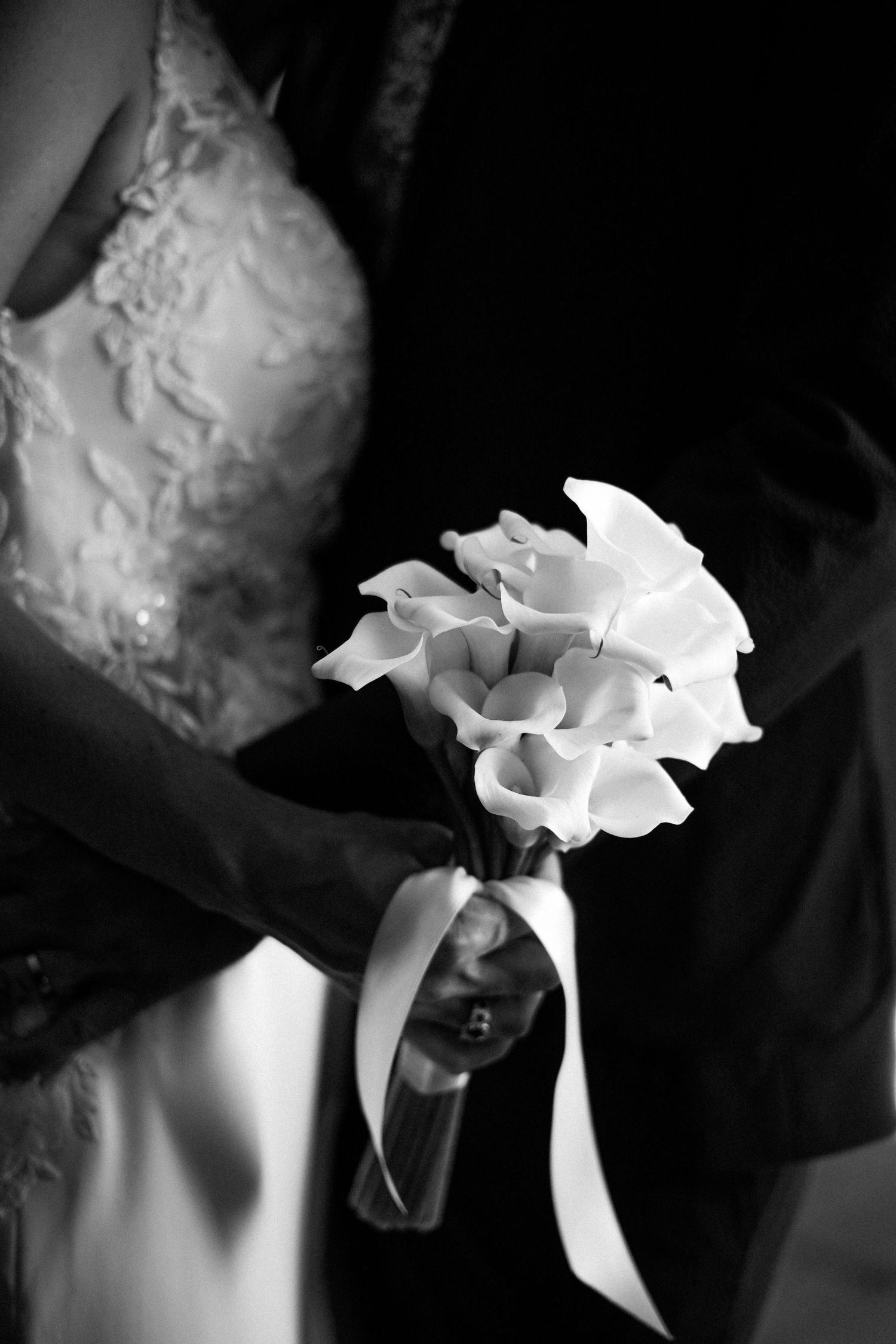 Elegant black and white close-up of a bridal bouquet of white calla lilies with ribbon.