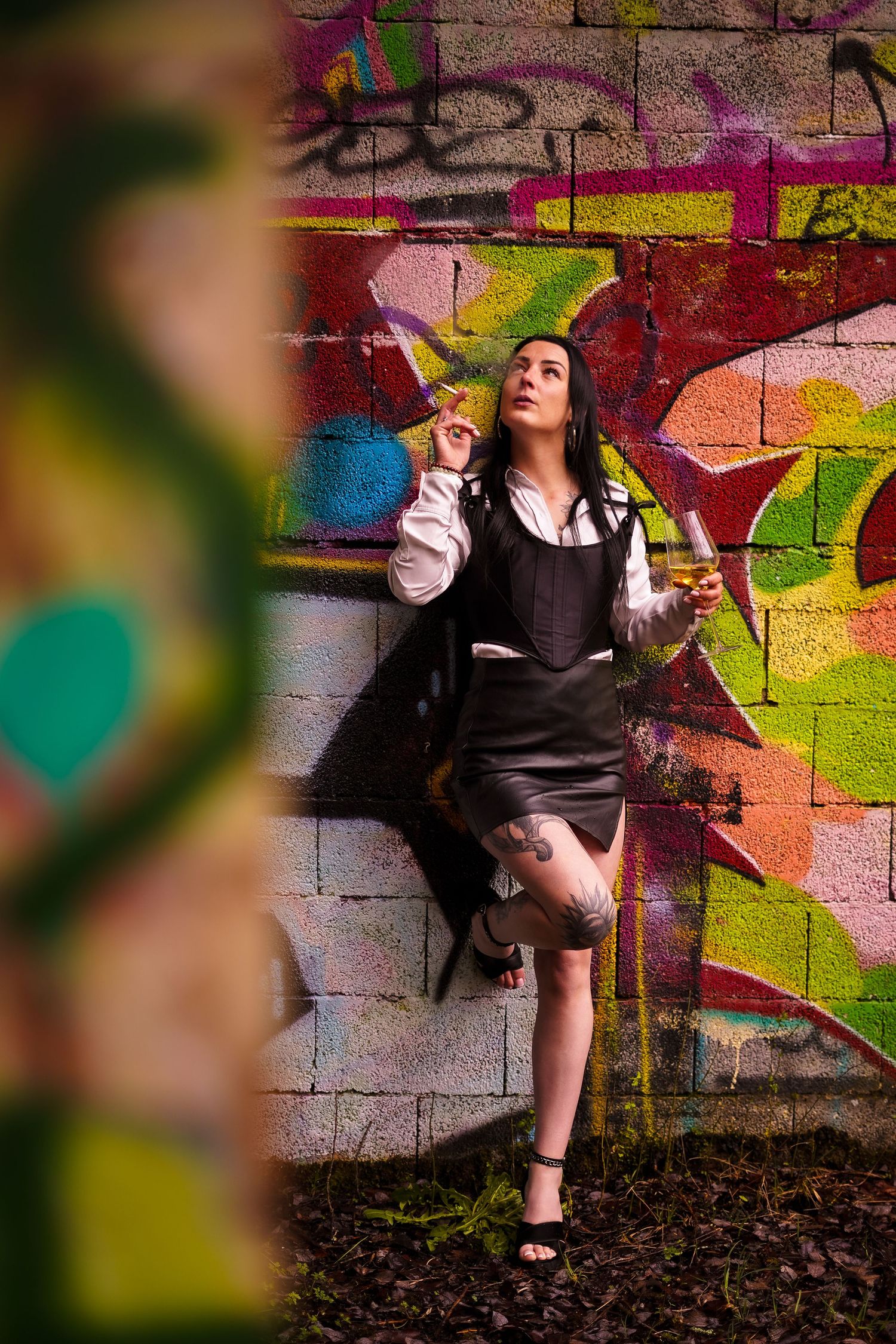 Stylish woman with cigar and drink poses against colorful graffiti wall.