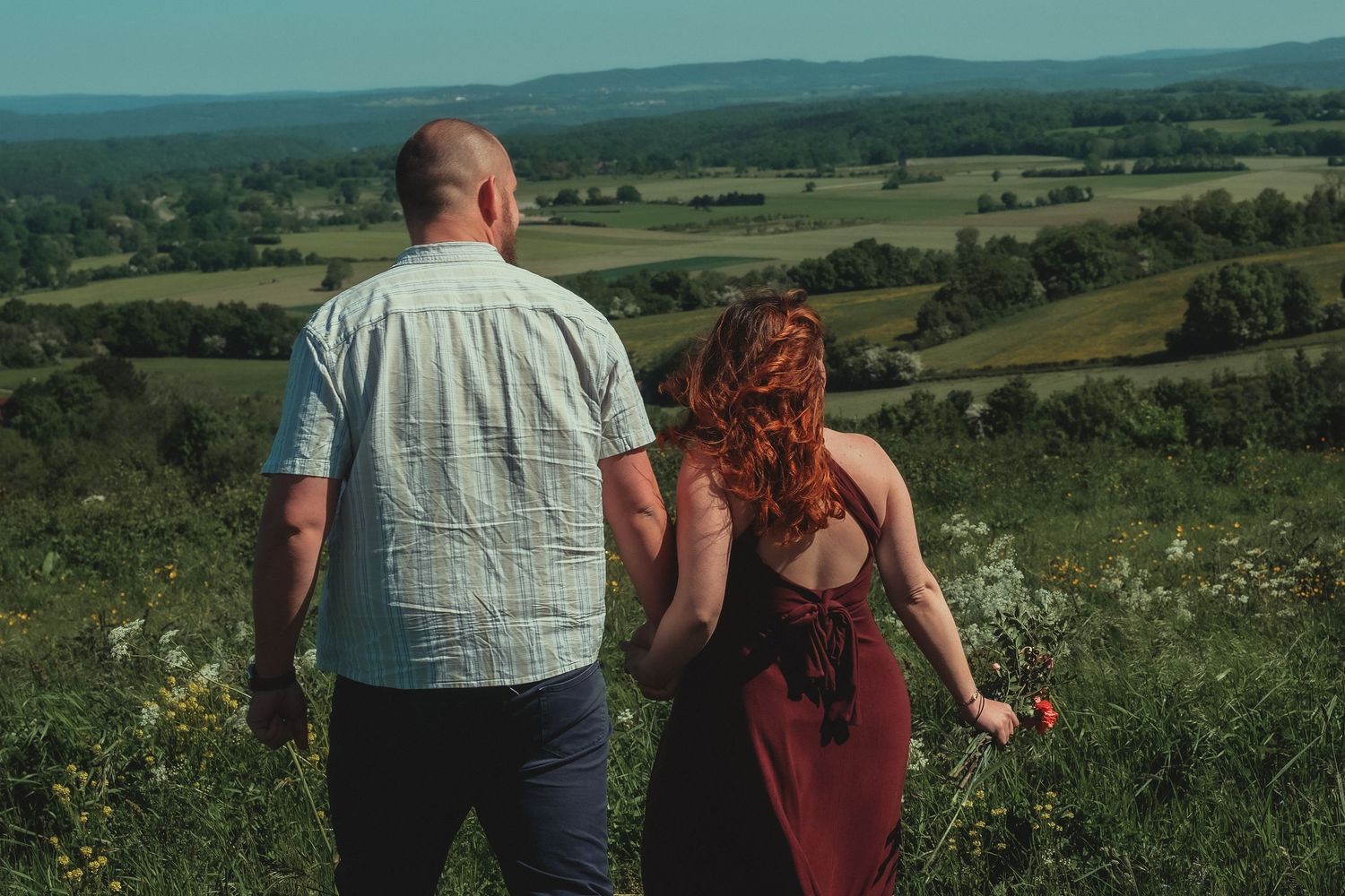 Couple holding hands overlooking lush green countryside valley on sunny summer day.