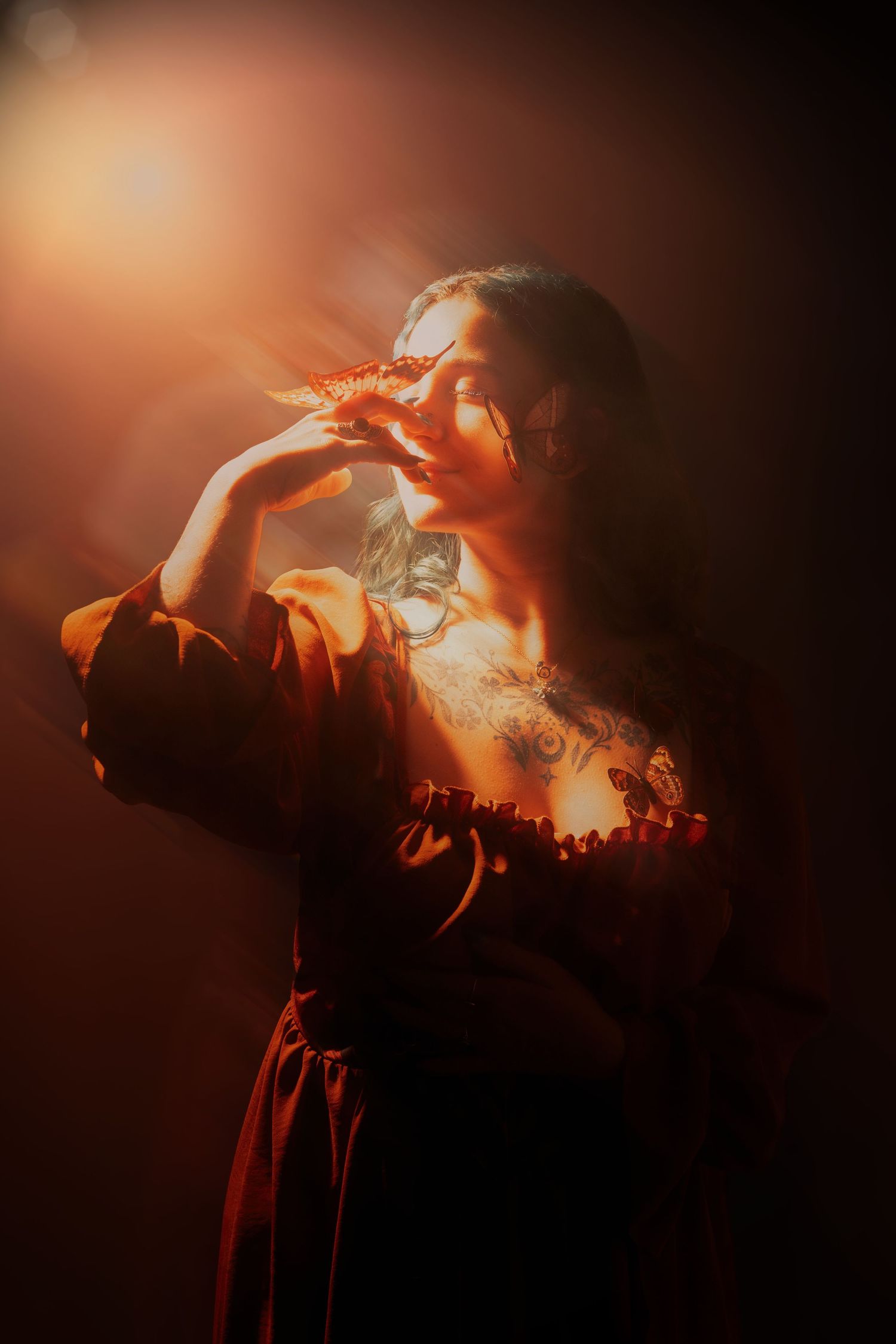 Woman in dark red dress holds decorative item near face, bathed in warm golden light with dramatic shadows.