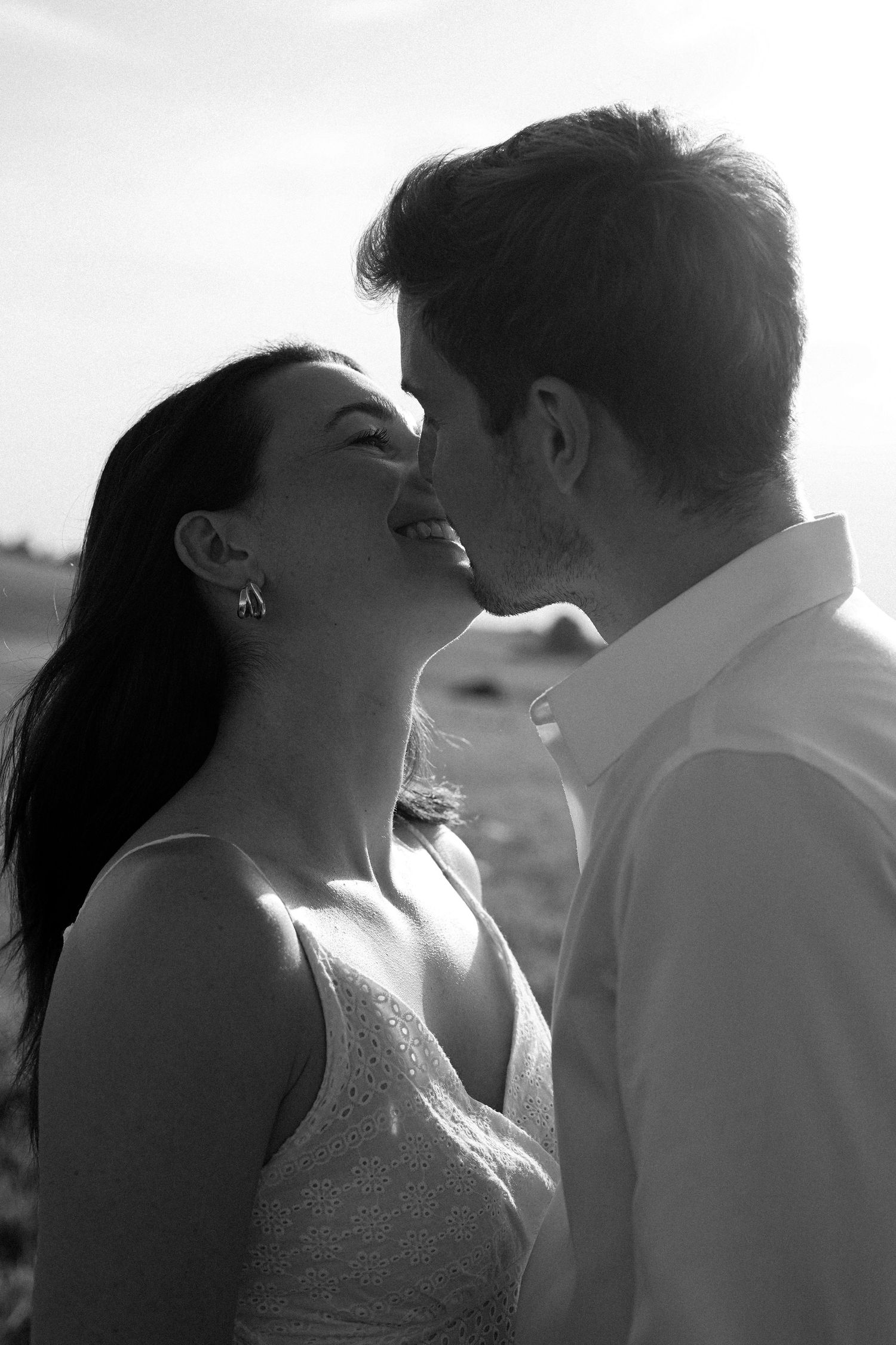 Black and white photo of smiling bride and groom sharing tender moment in sunlight.