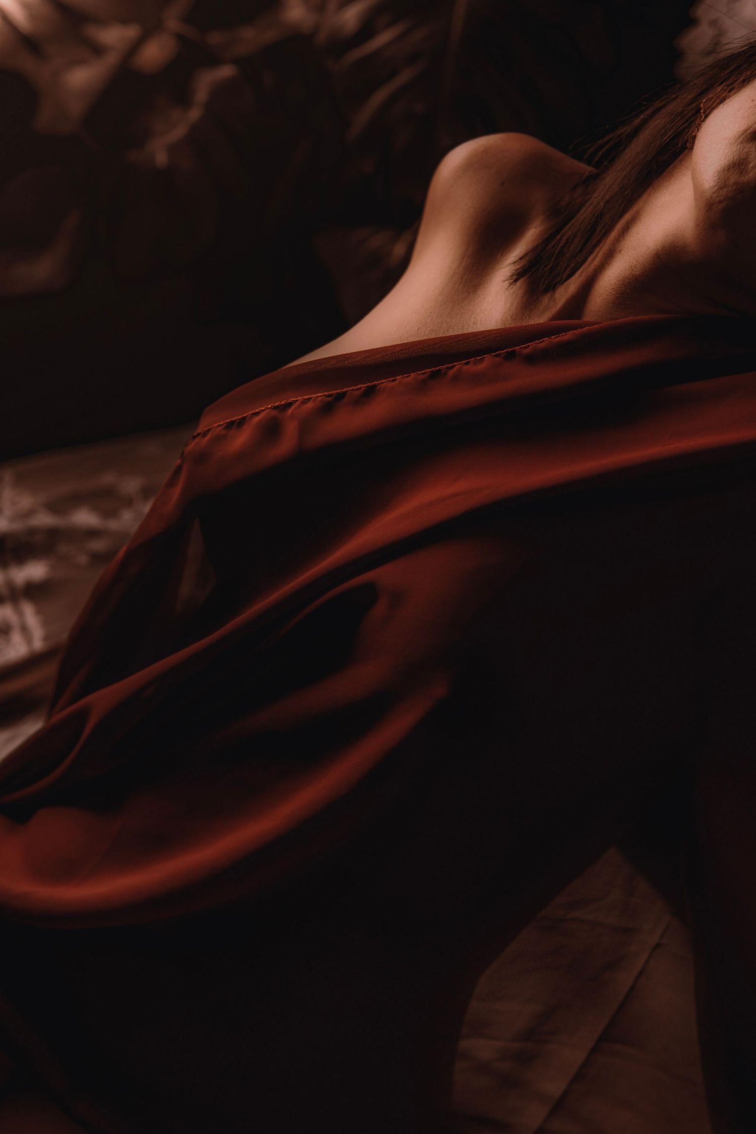 Sensual artistic photo of a bare back with flowing deep red silk fabric in moody low-key lighting.