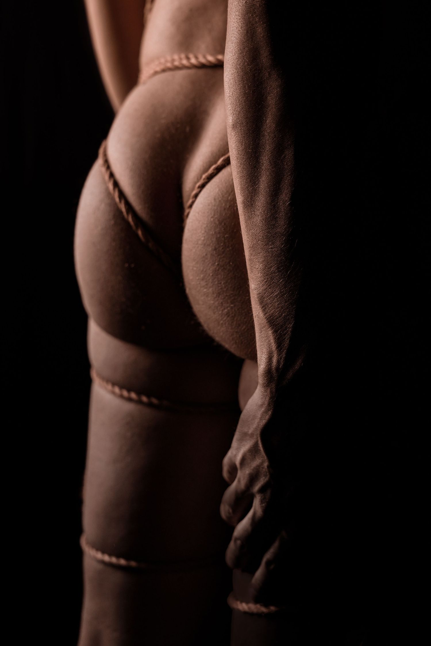 Close-up of woman in rope bondage lingerie against black background highlighting body curves.