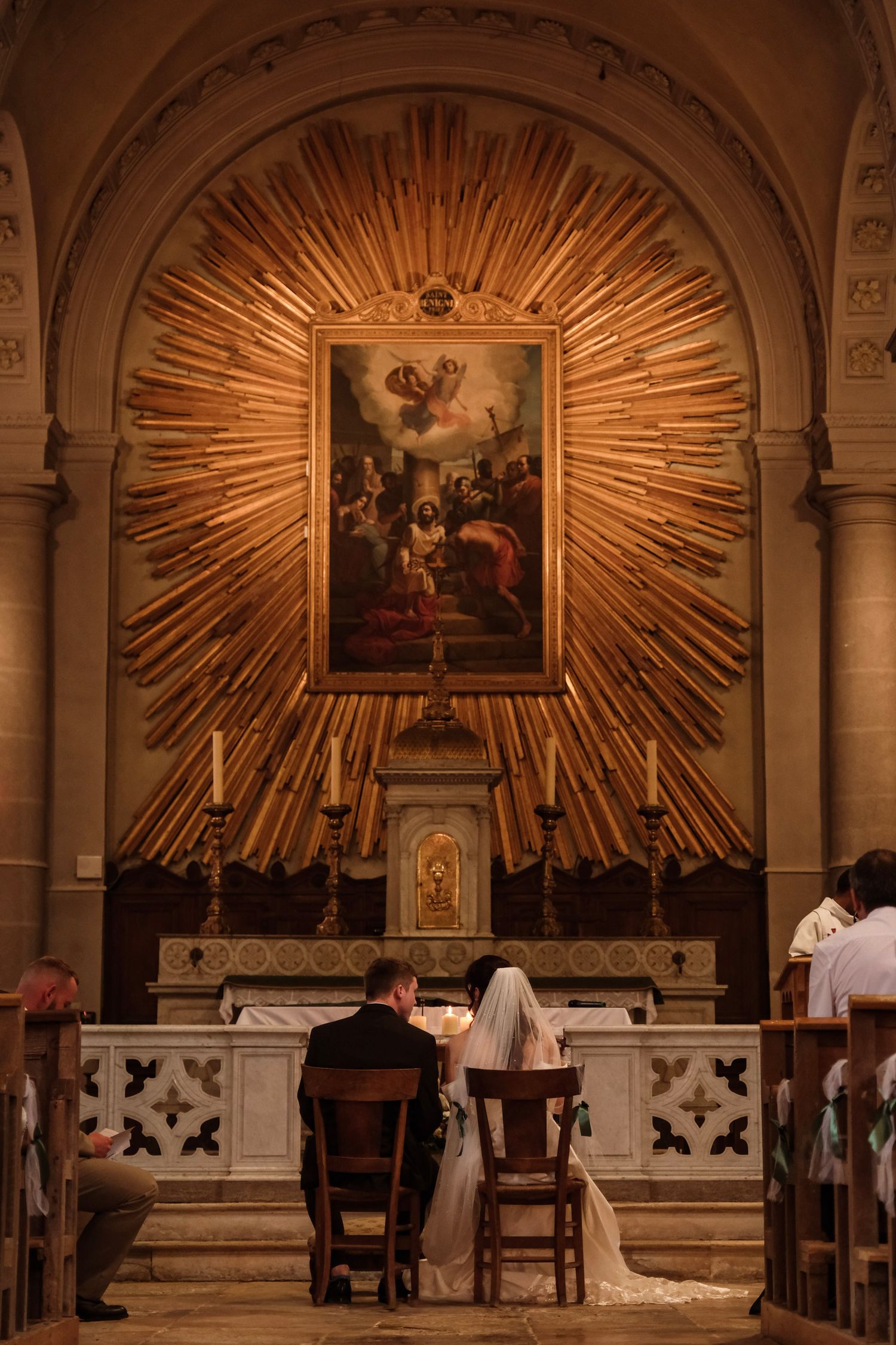 Bride and groom sit before a stunning golden sunburst altar during their church wedding ceremony.
