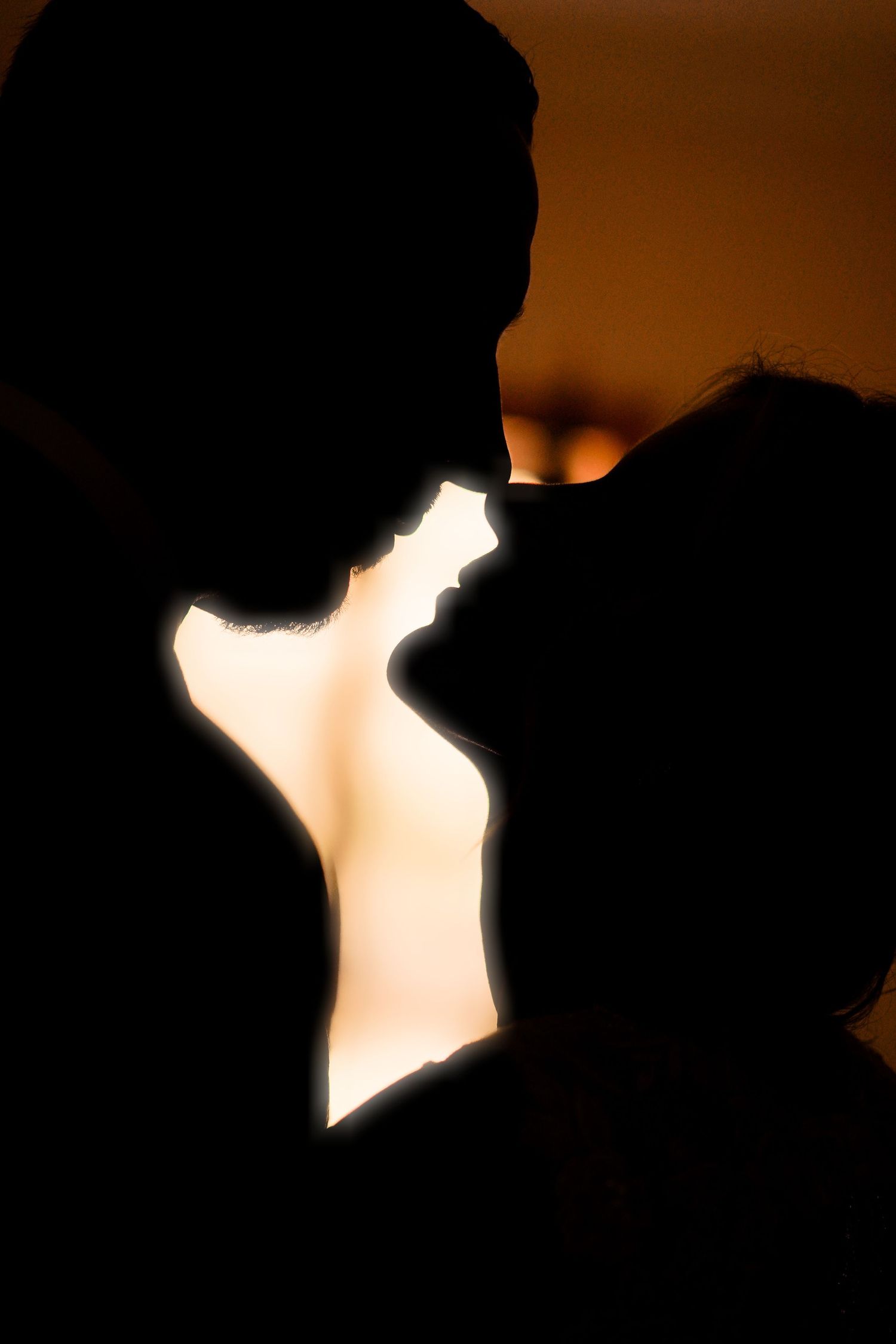 Romantic silhouette of couple about to kiss against warm golden backlit background.