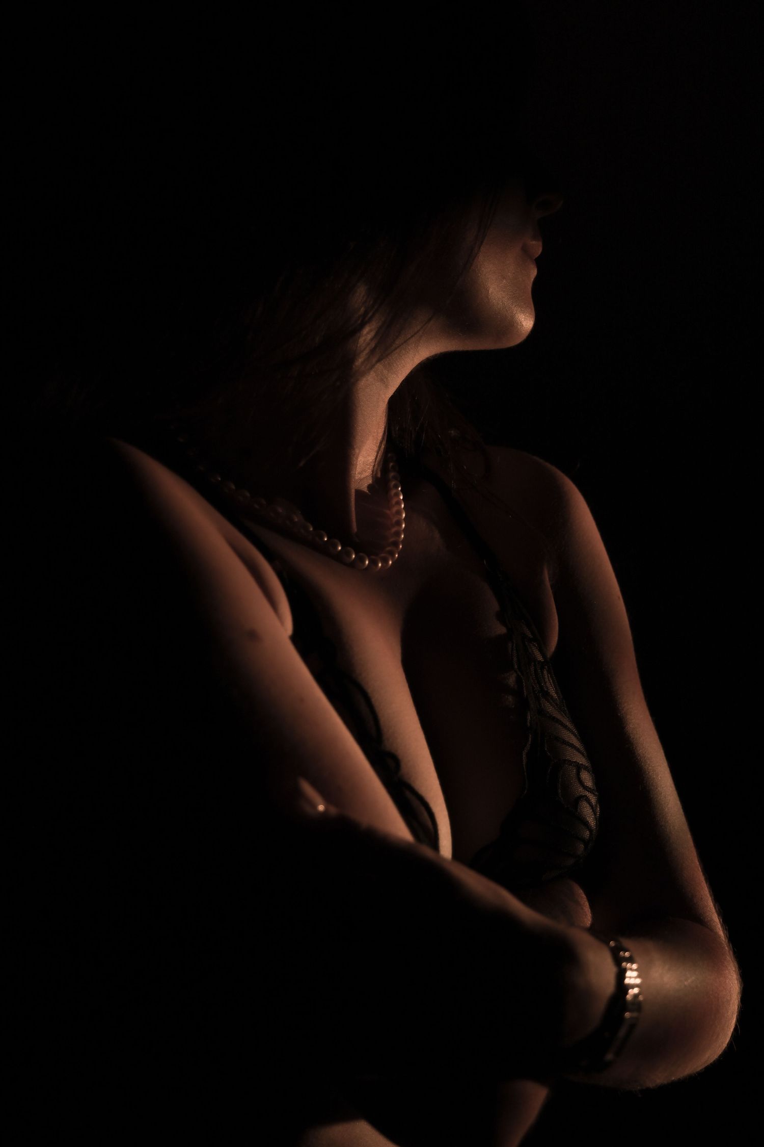 Silhouette of a woman wearing a pearl necklace and bracelet posed in dramatic low-key lighting against a dark background.