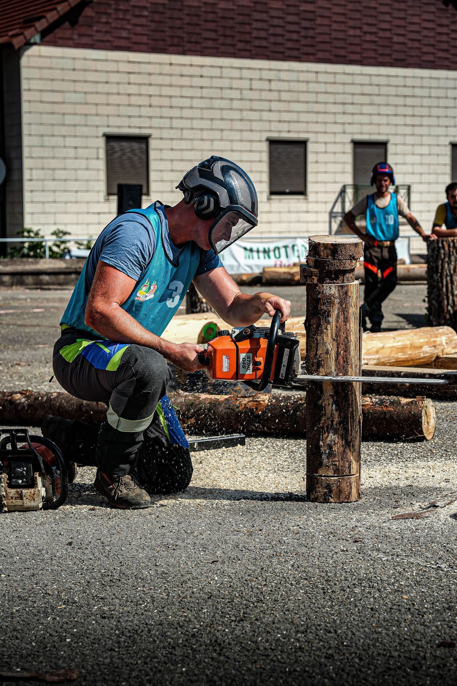 Professional lumberjack using chainsaw on logs during outdoor woodcutting competition in safety gear.