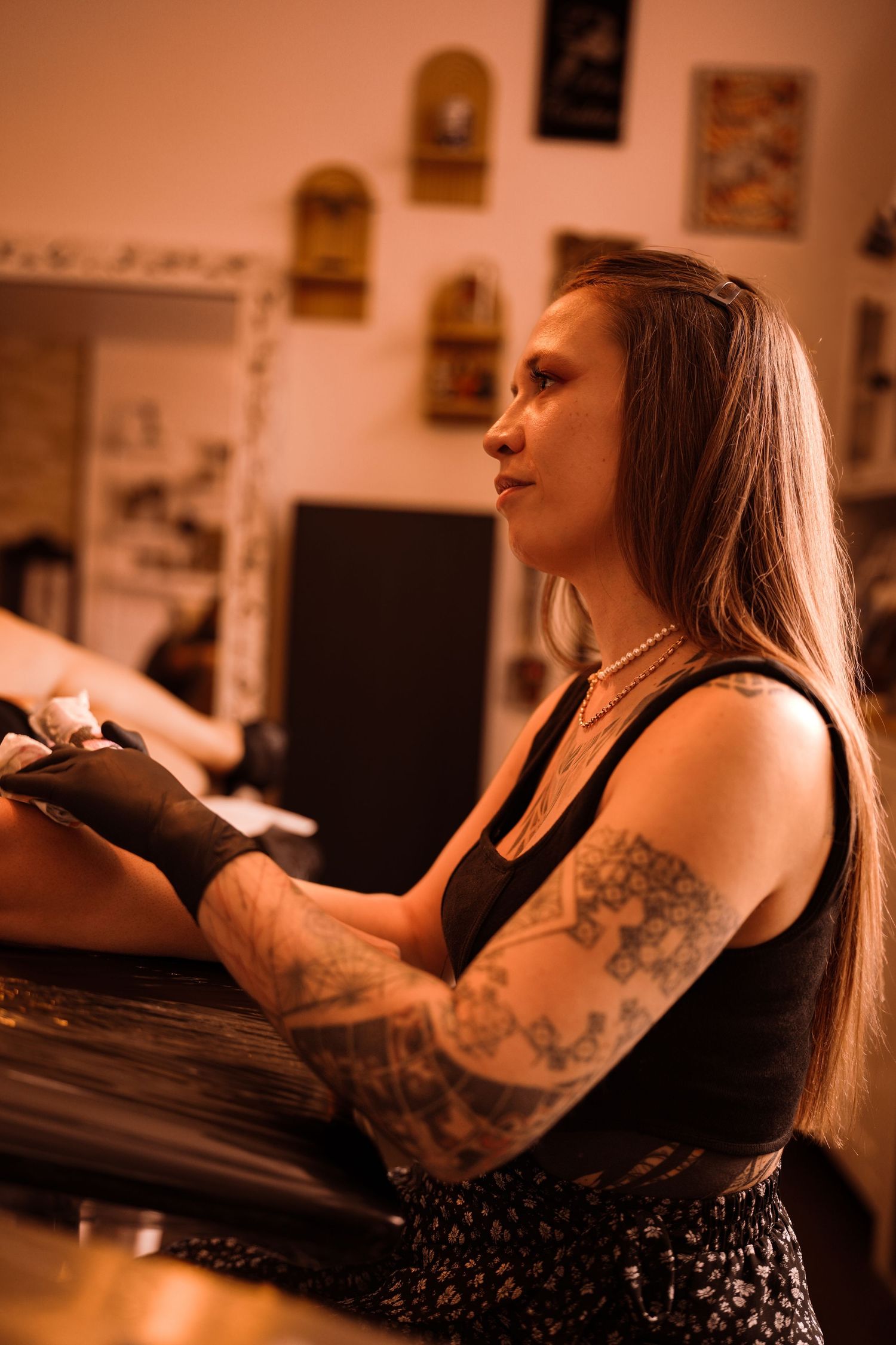 Tattooed female tattoo artist working at her station in a warmly lit tattoo studio.