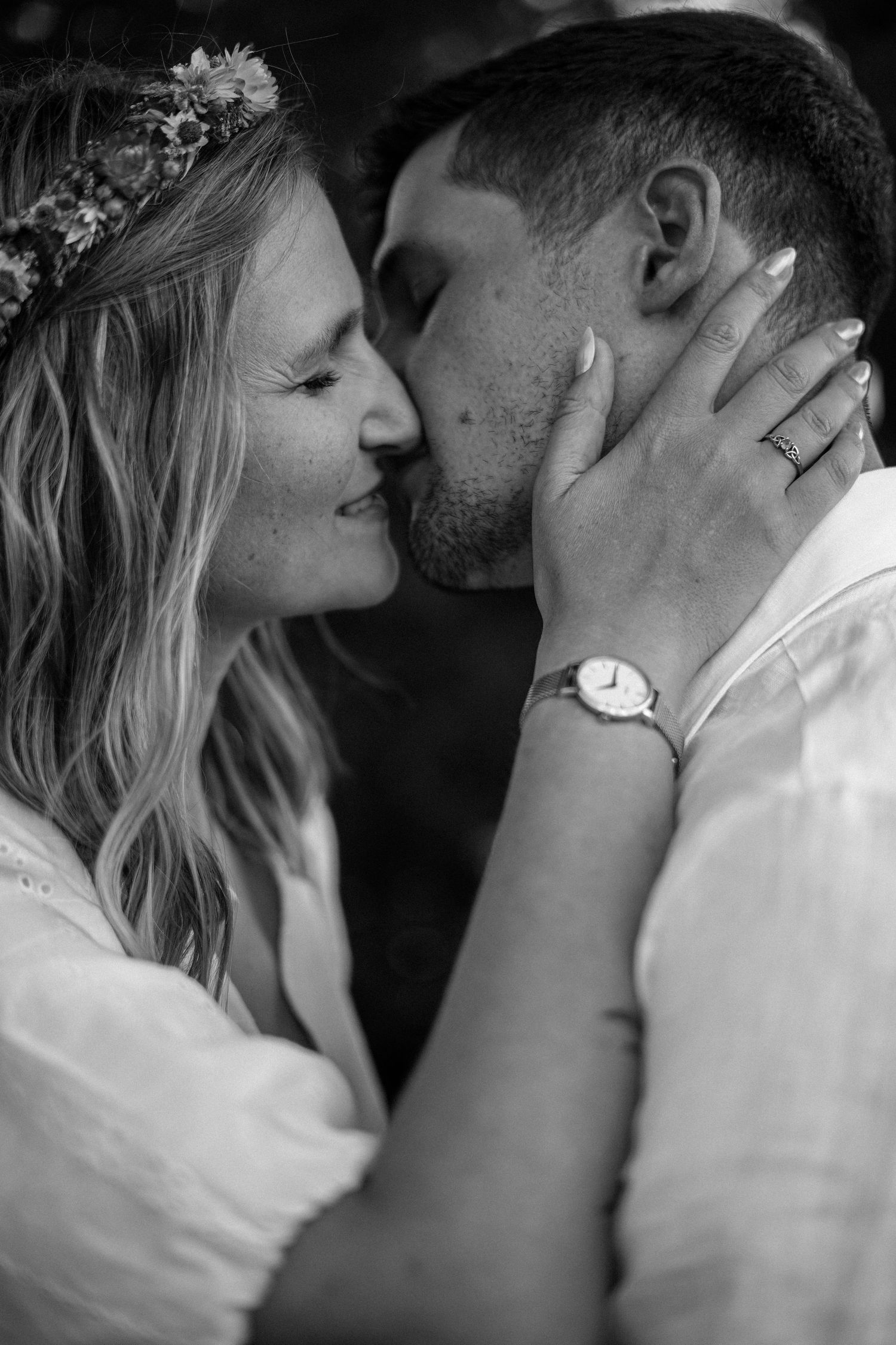Black and white close-up of a bride and groom sharing a kiss, bride wearing a floral crown.