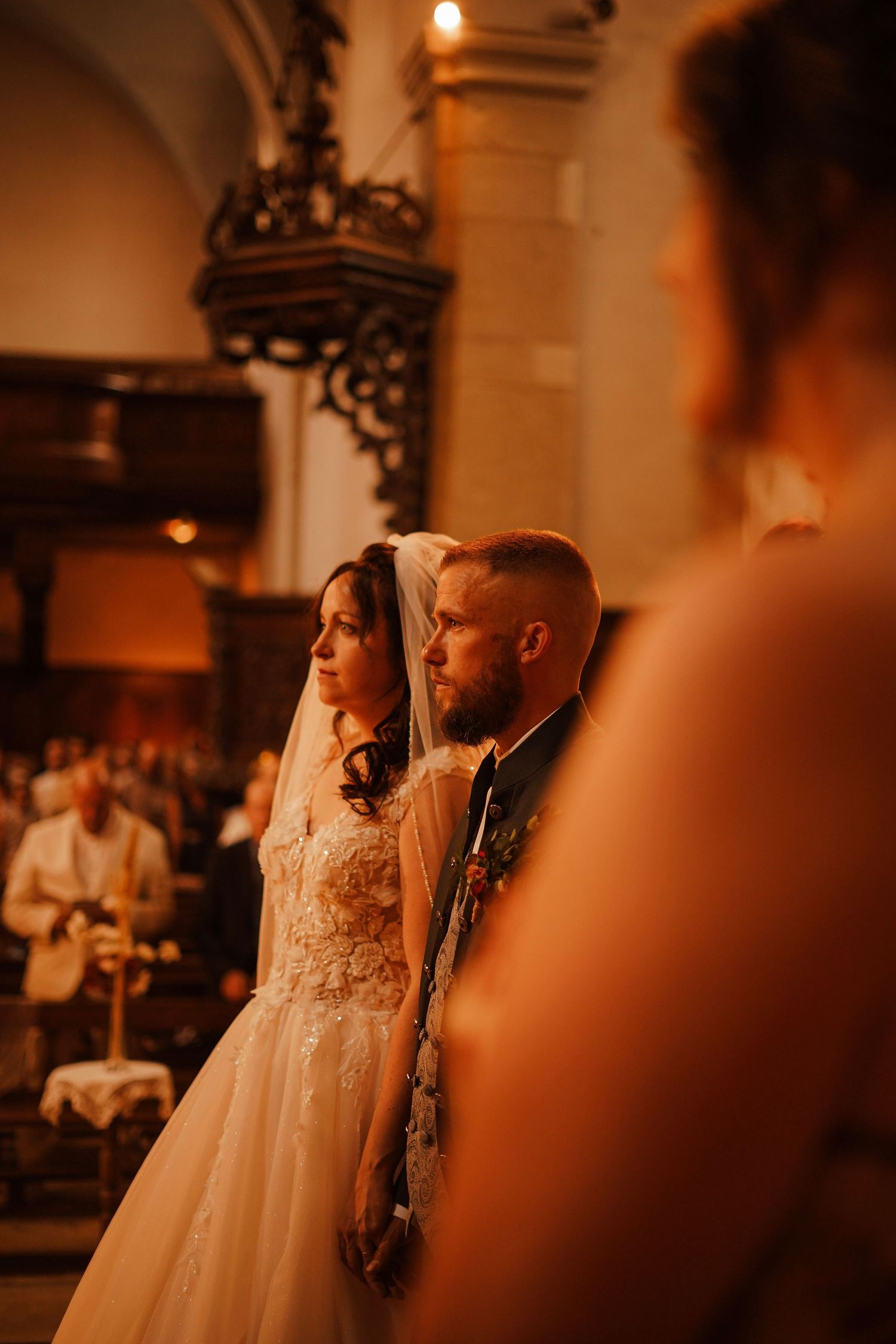 Bride and groom standing solemnly together during wedding ceremony inside an ornate historic church.