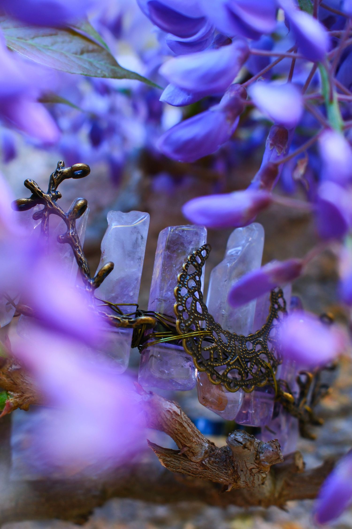 Close-up of an ornate bronze and crystal jewelry piece surrounded by vibrant purple wisteria flowers.