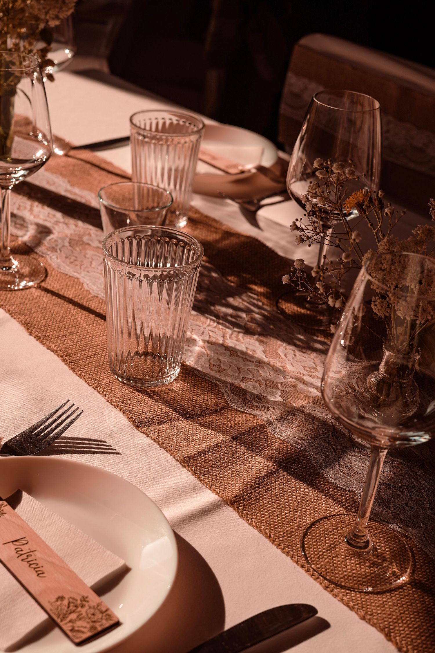 Elegant wedding reception table setting with crystal glasses and burlap runner in warm light.