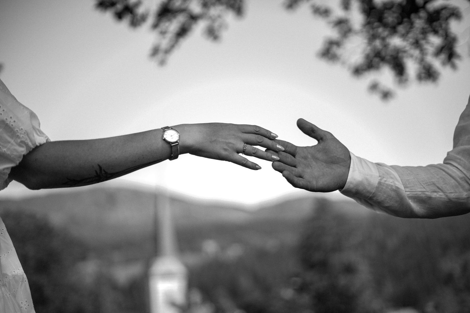 Black and white photo of bride and groom touching hands with a church steeple in the background.