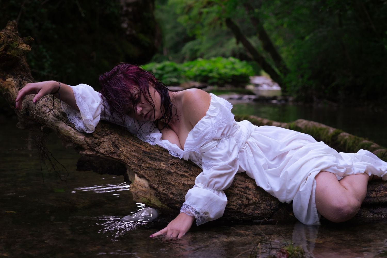 Woman in white dress lying on a log in a forest stream, ethereal nature photography.