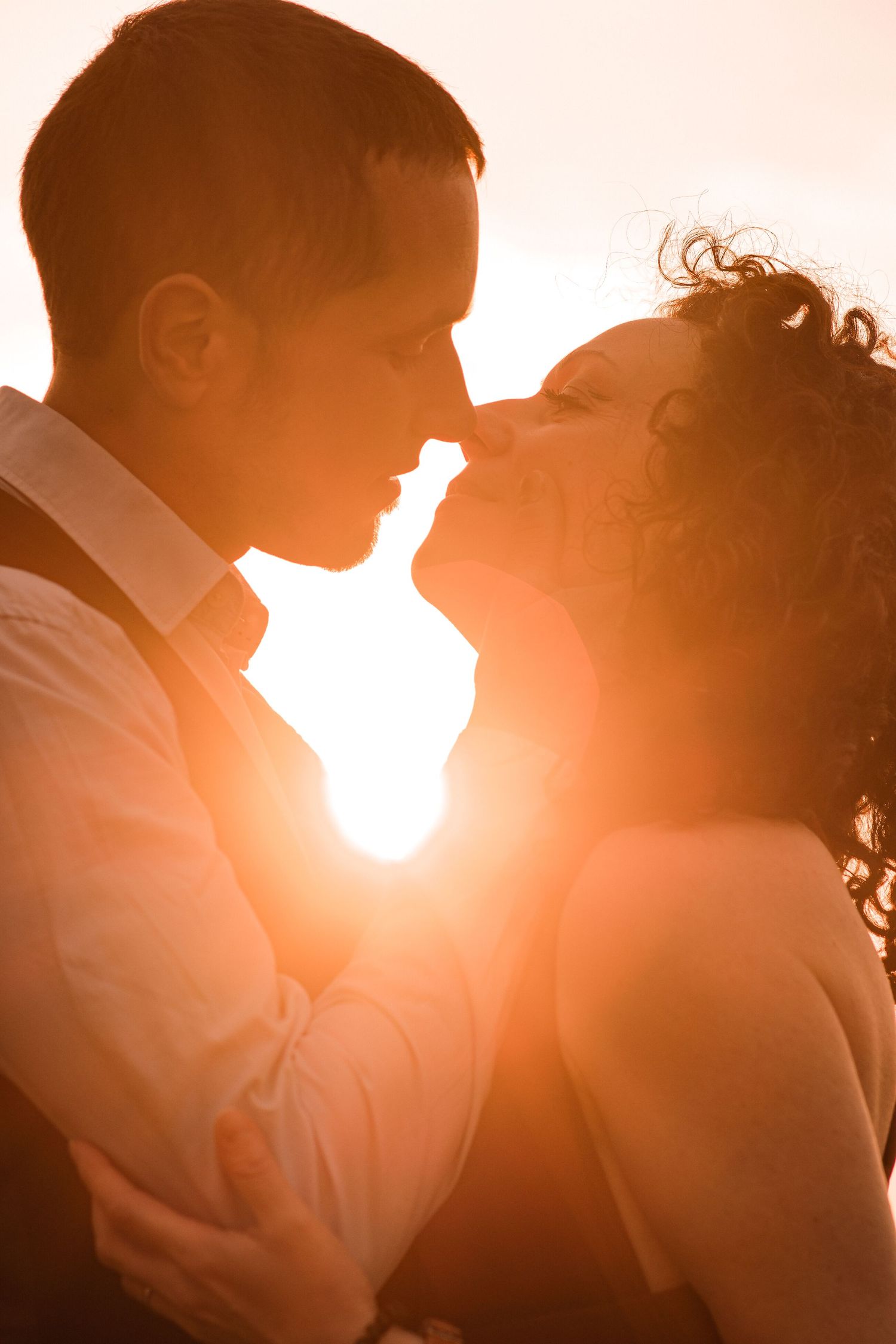 Romantic couple sharing an intimate moment, nearly kissing, bathed in warm golden sunset backlight.