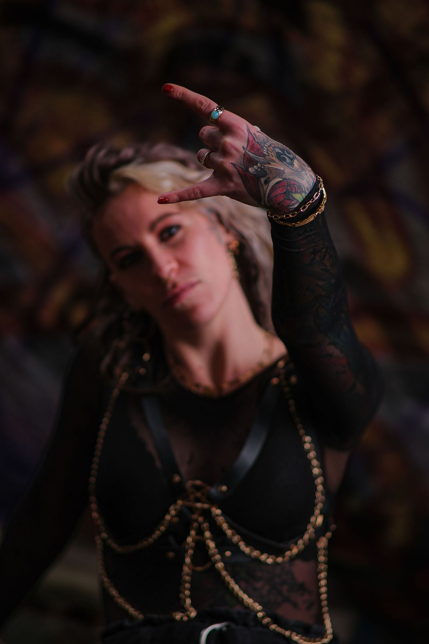 Tattooed woman in dark outfit making hand gesture with dramatic artistic background.