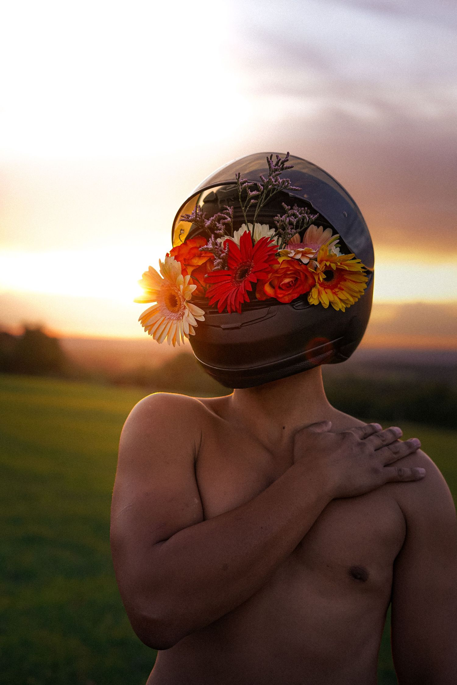 Shirtless person wearing a motorcycle helmet filled with colorful flowers at sunset.
