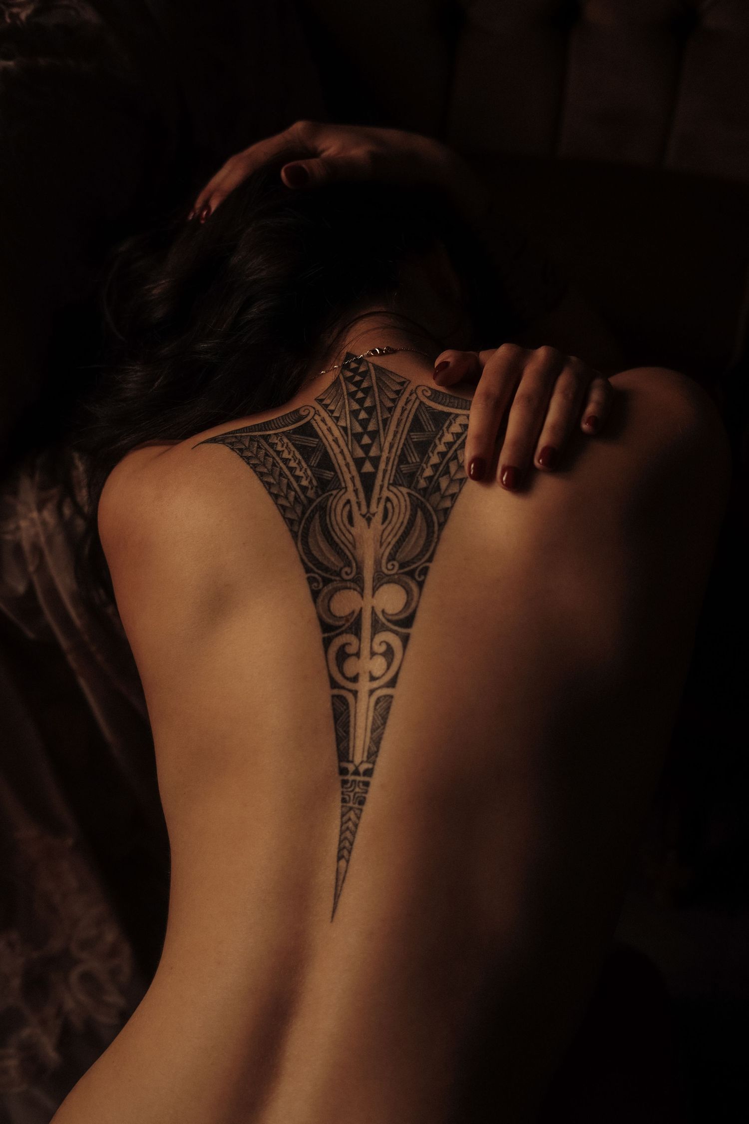 Woman with intricate tribal spine tattoo on her back in moody dark lighting.