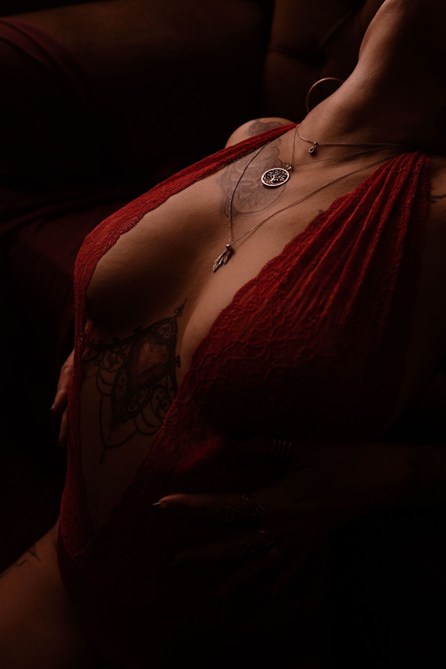 Close-up of woman in deep red dress with chest tattoo and silver pendant necklaces.