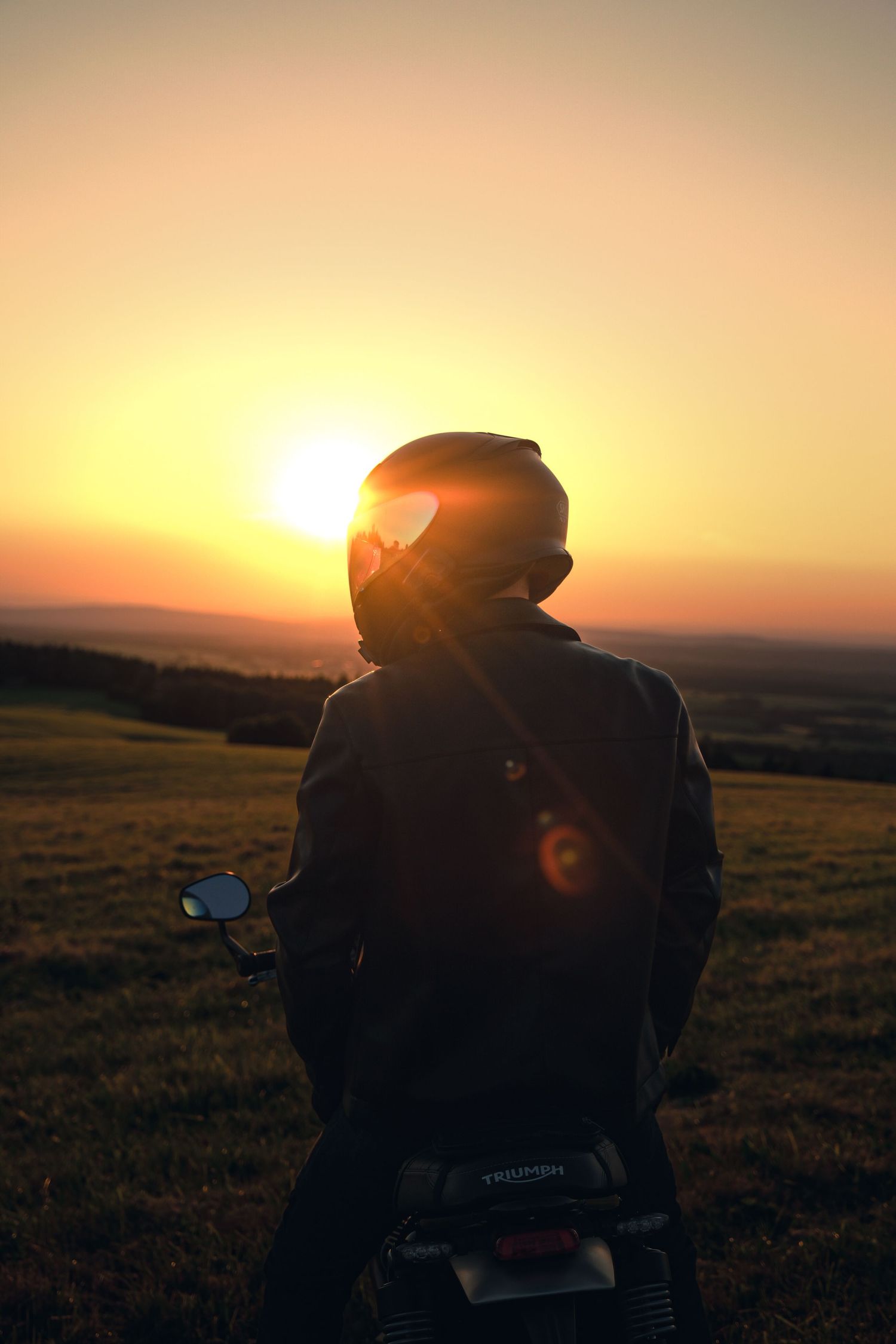 Motorcyclist in helmet silhouetted against stunning golden sunset landscape.