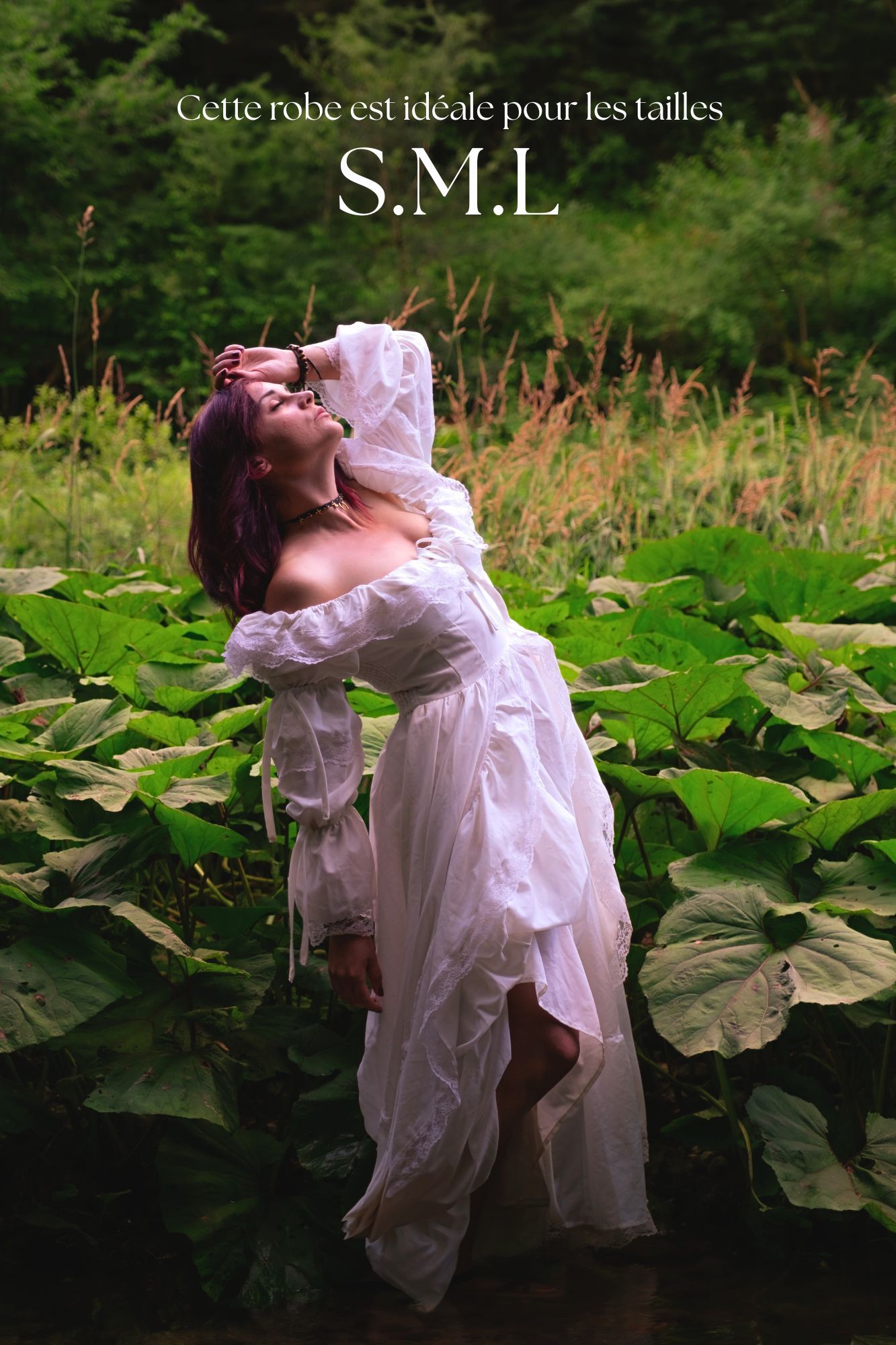 Woman in white flowing dress poses among large green leaves in a lush garden, available in sizes S, M, and L.