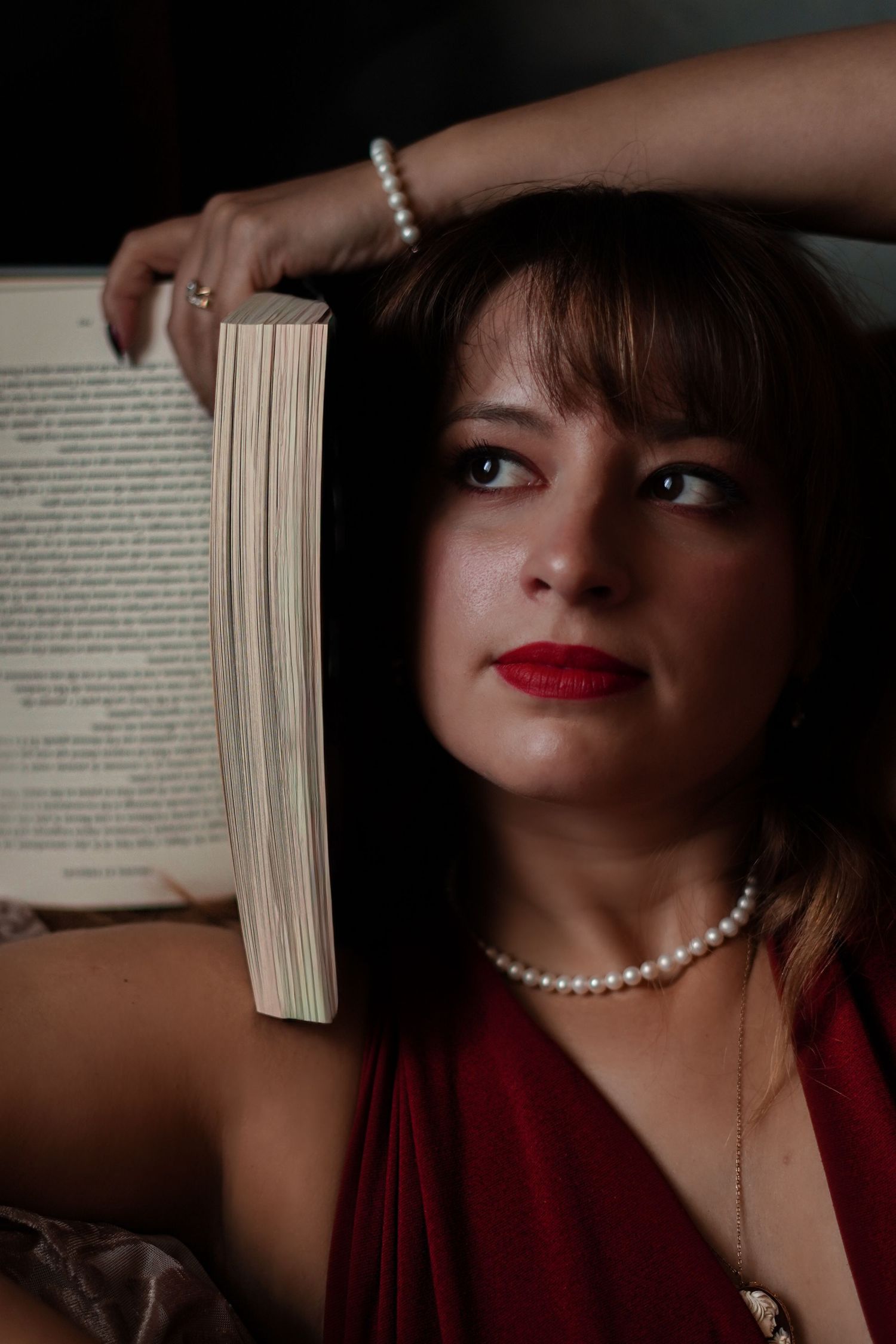 Woman in red dress holding book with pearl necklace and bracelet posing for portrait photo.