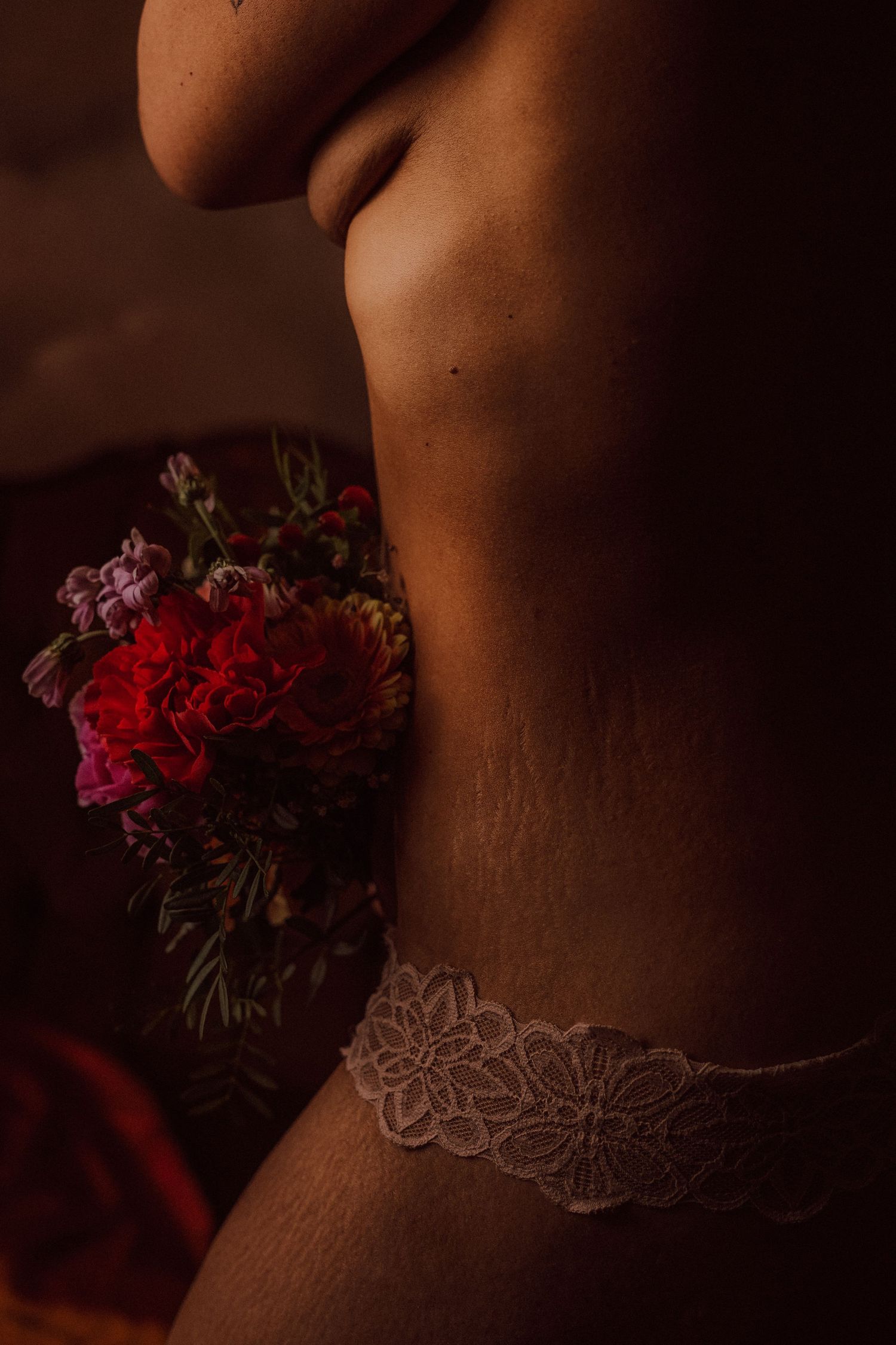 Close-up of woman in white lace underwear holding red flowers against her hip.