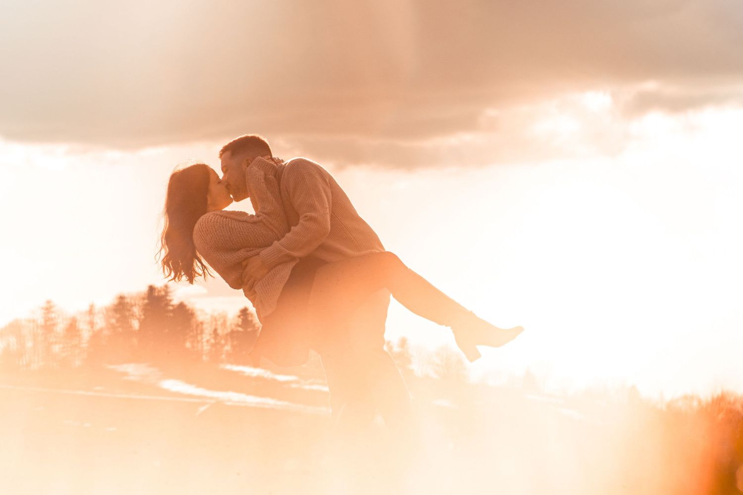 Couple sharing a romantic dip kiss silhouetted against a bright glowing sunset sky.