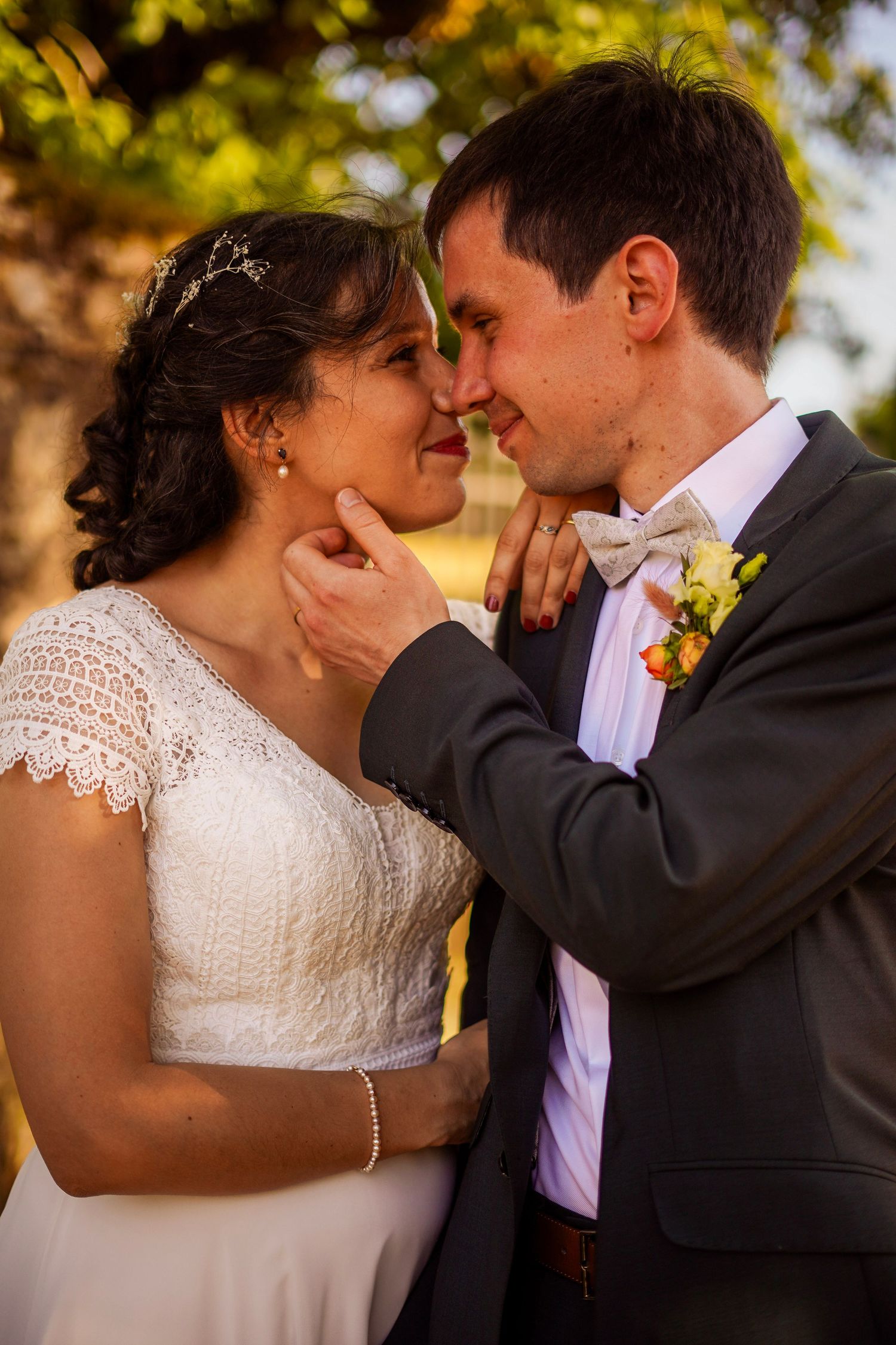 Groom tenderly holds bride's face as they share an intimate moment outdoors in warm golden light.