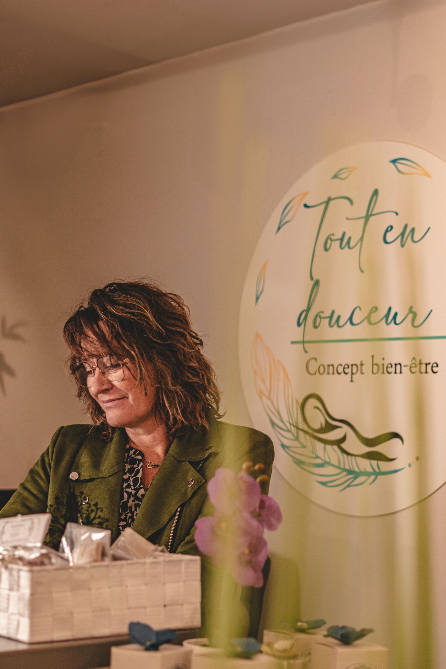 Woman in green jacket smiling at wellness concept booth with Tout en Douceur branded banner.