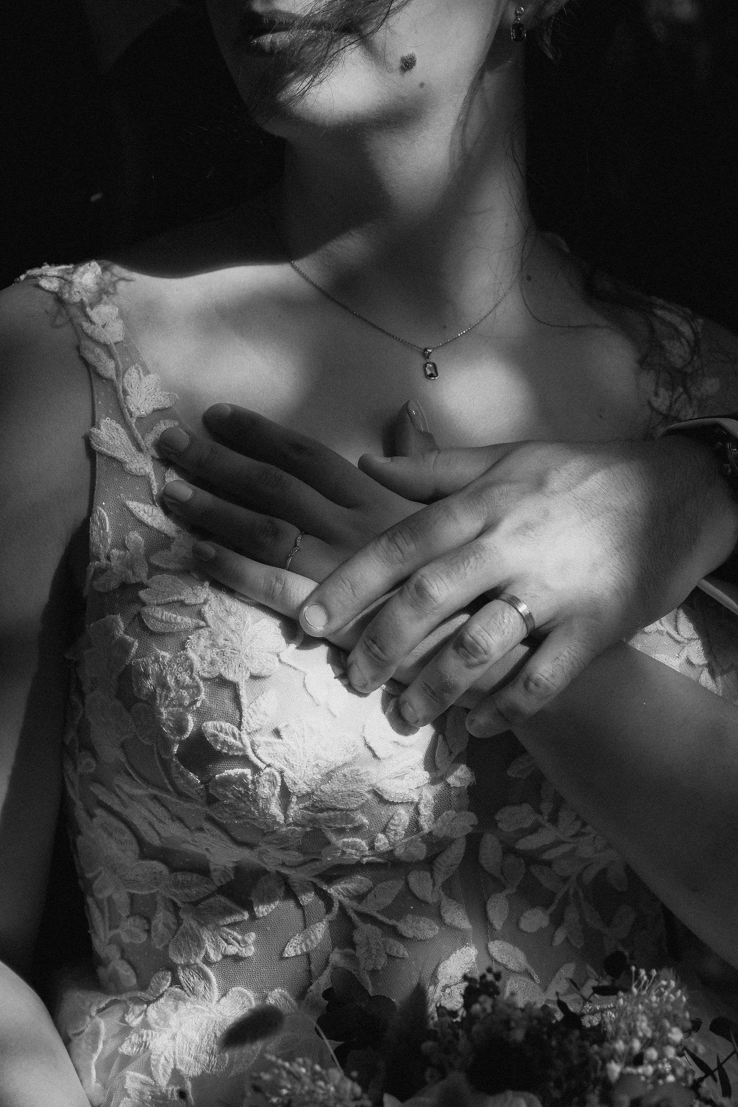 Black and white close-up of a bride in lace dress wearing a wedding ring and delicate necklace.