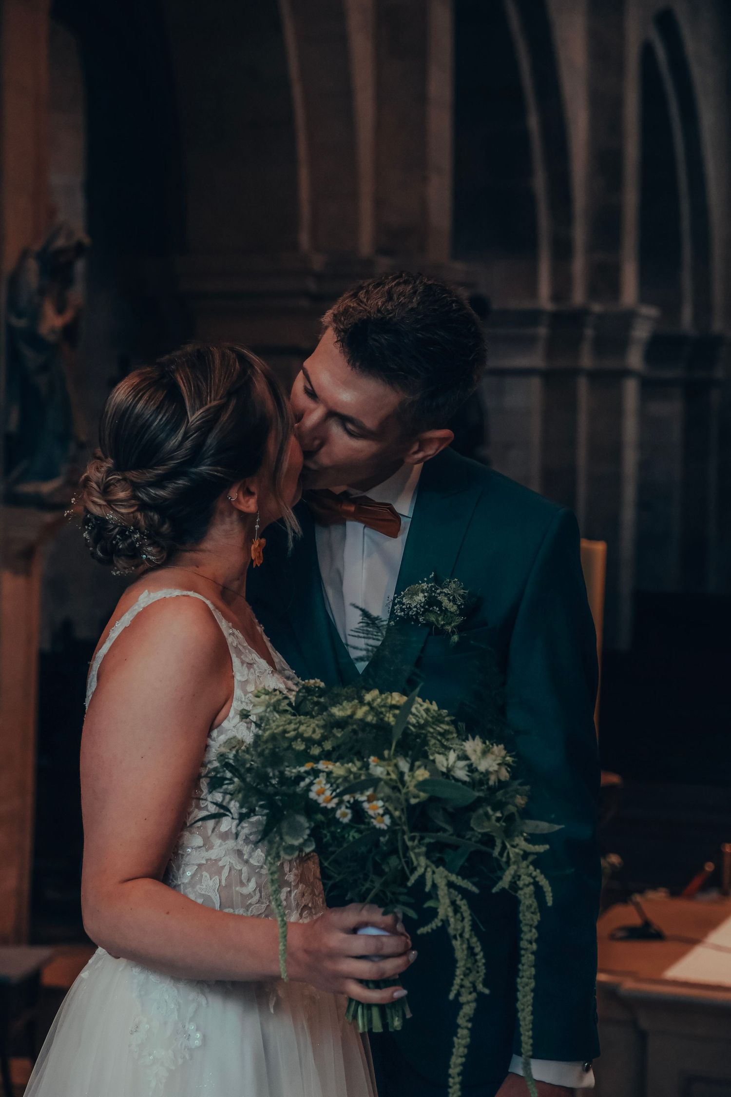 Bride and groom share a tender kiss inside a historic church holding a white floral bouquet.