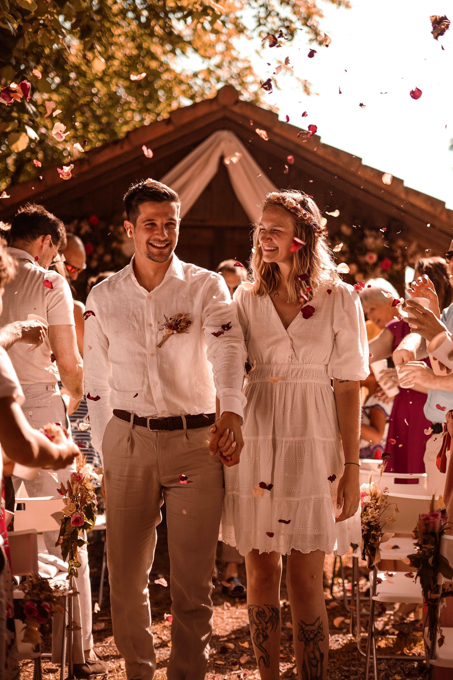 Joyful bride and groom walk down the aisle as guests shower them with rose petals outdoors.