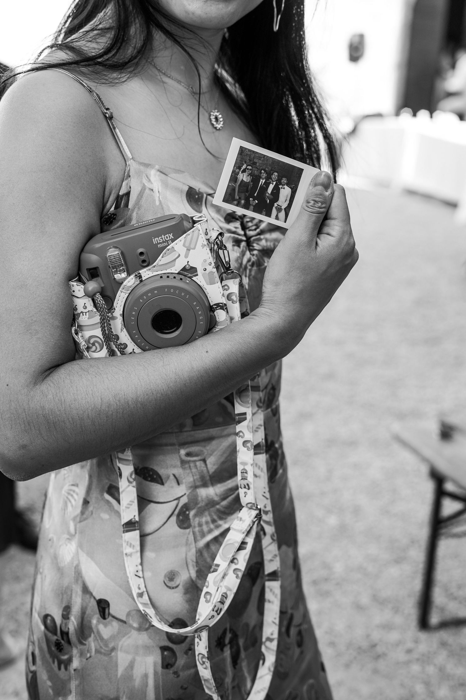 Wedding guest holding Instax camera and polaroid photo in black and white at reception.