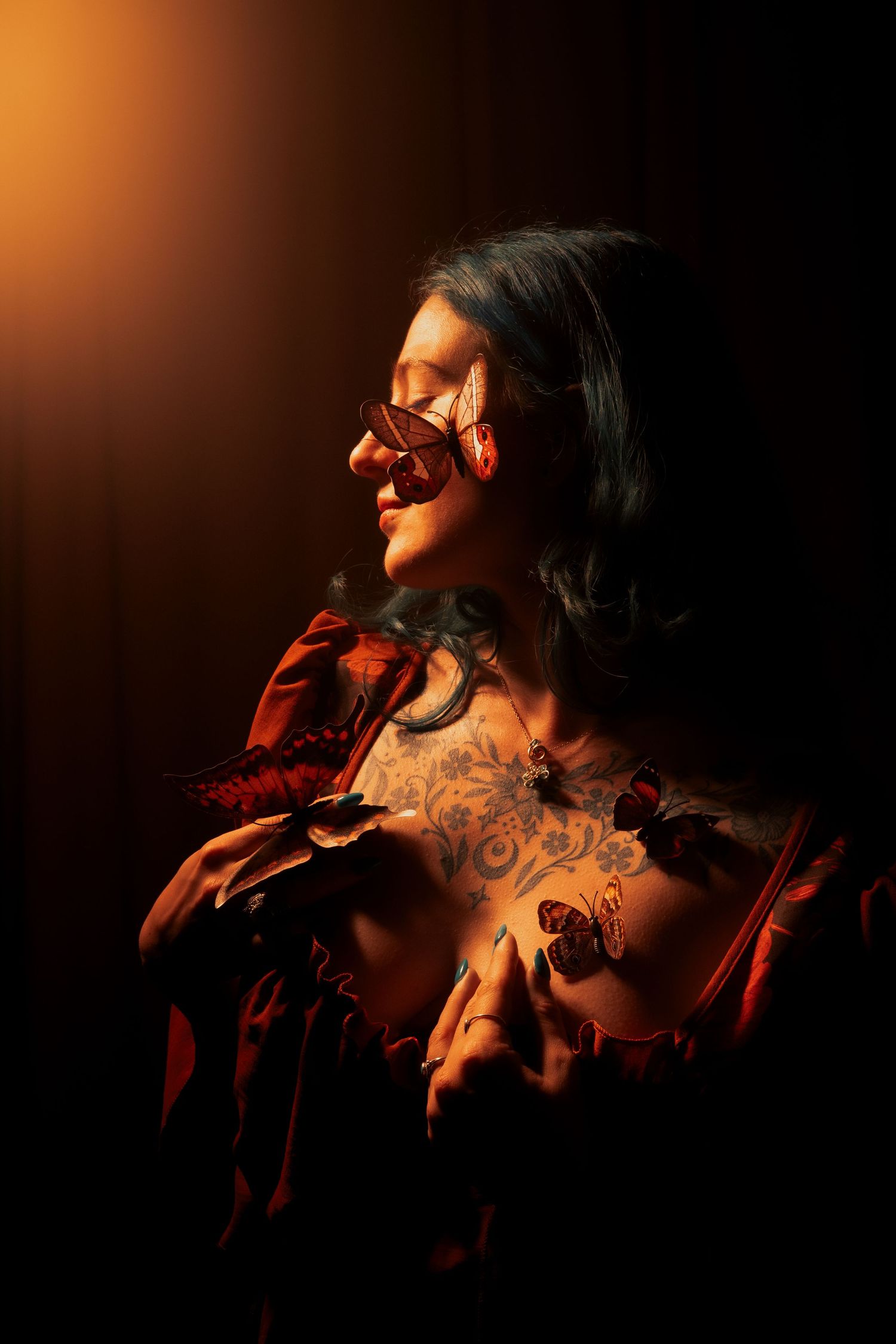 Tattooed woman in red dress adorned with butterflies posing in dramatic warm golden light.