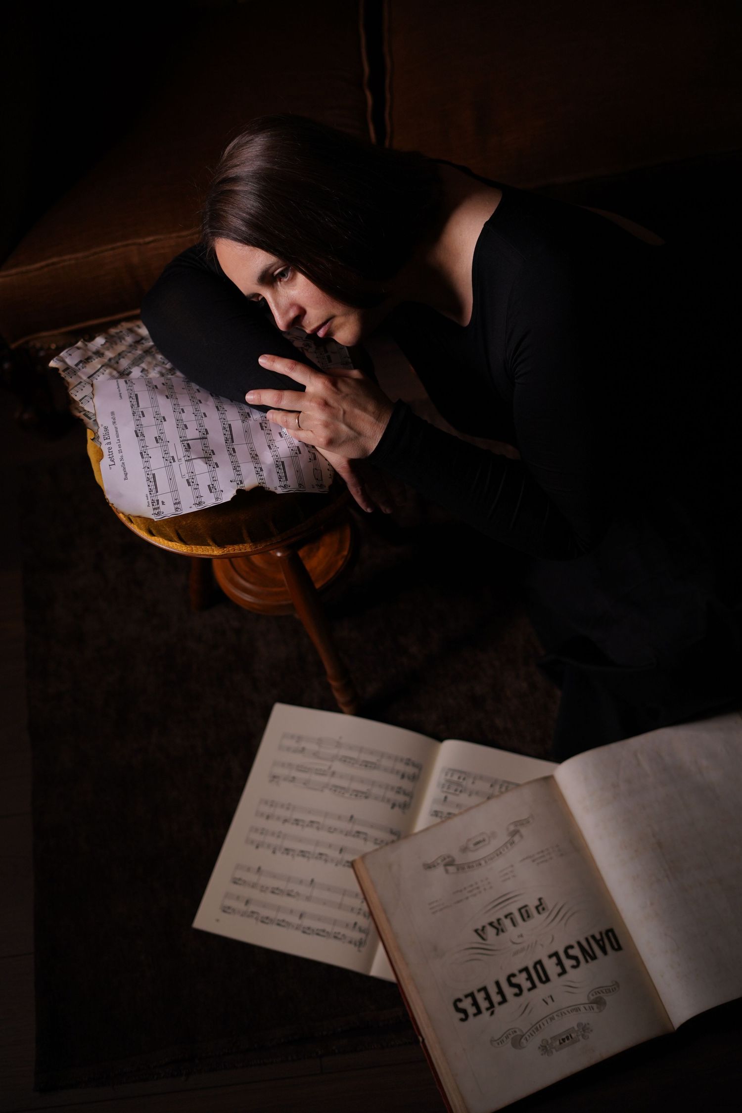 Woman in black dress reading sheet music in dark moody lighting with vintage Polka book.