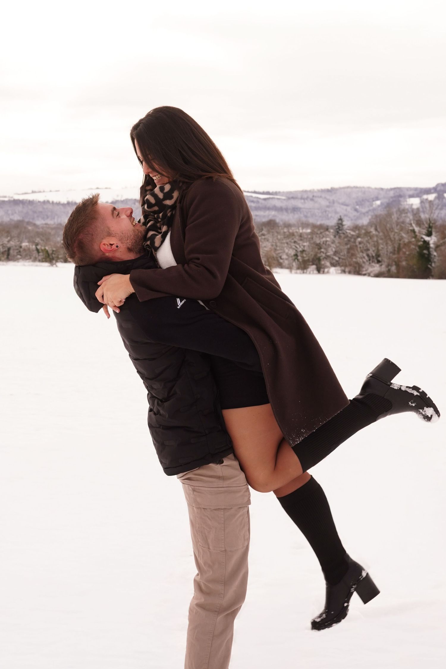 Man lifting woman in a loving embrace in a snowy winter landscape.