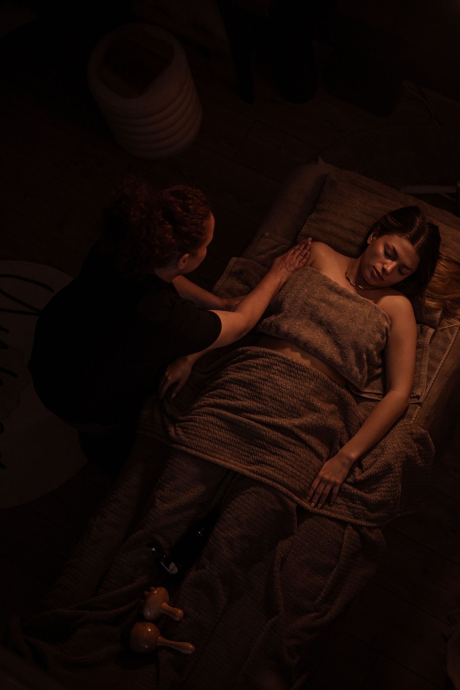 Massage therapist performing a body massage on a woman lying on a table in a candlelit room.