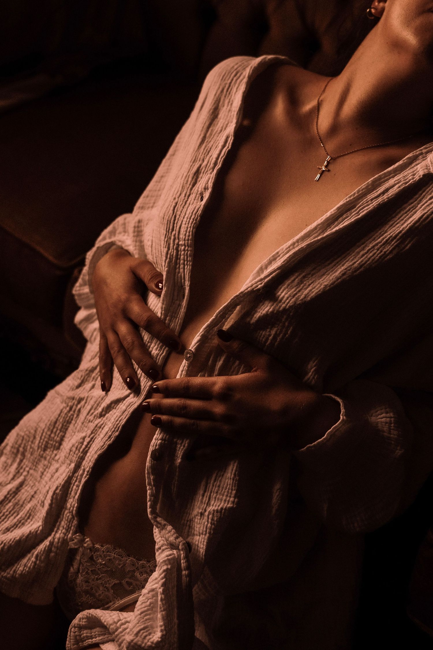 Woman in open linen robe with cross necklace in warm-toned intimate boudoir photography session.